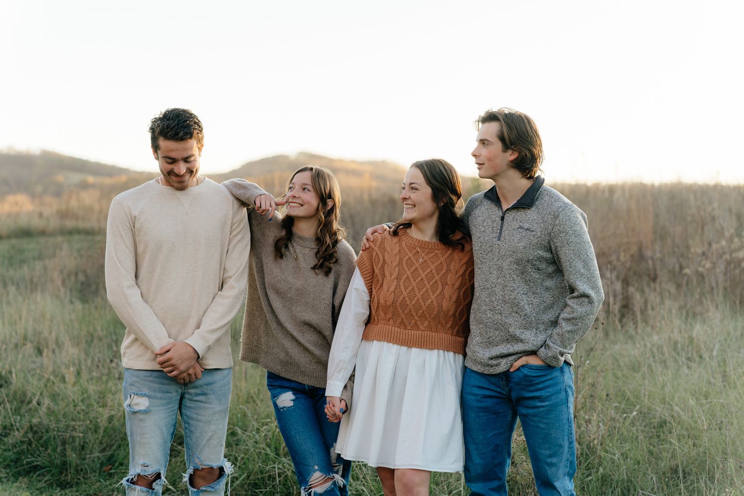 Group of friends laughing together in casual sweaters against autumn field backdrop.
