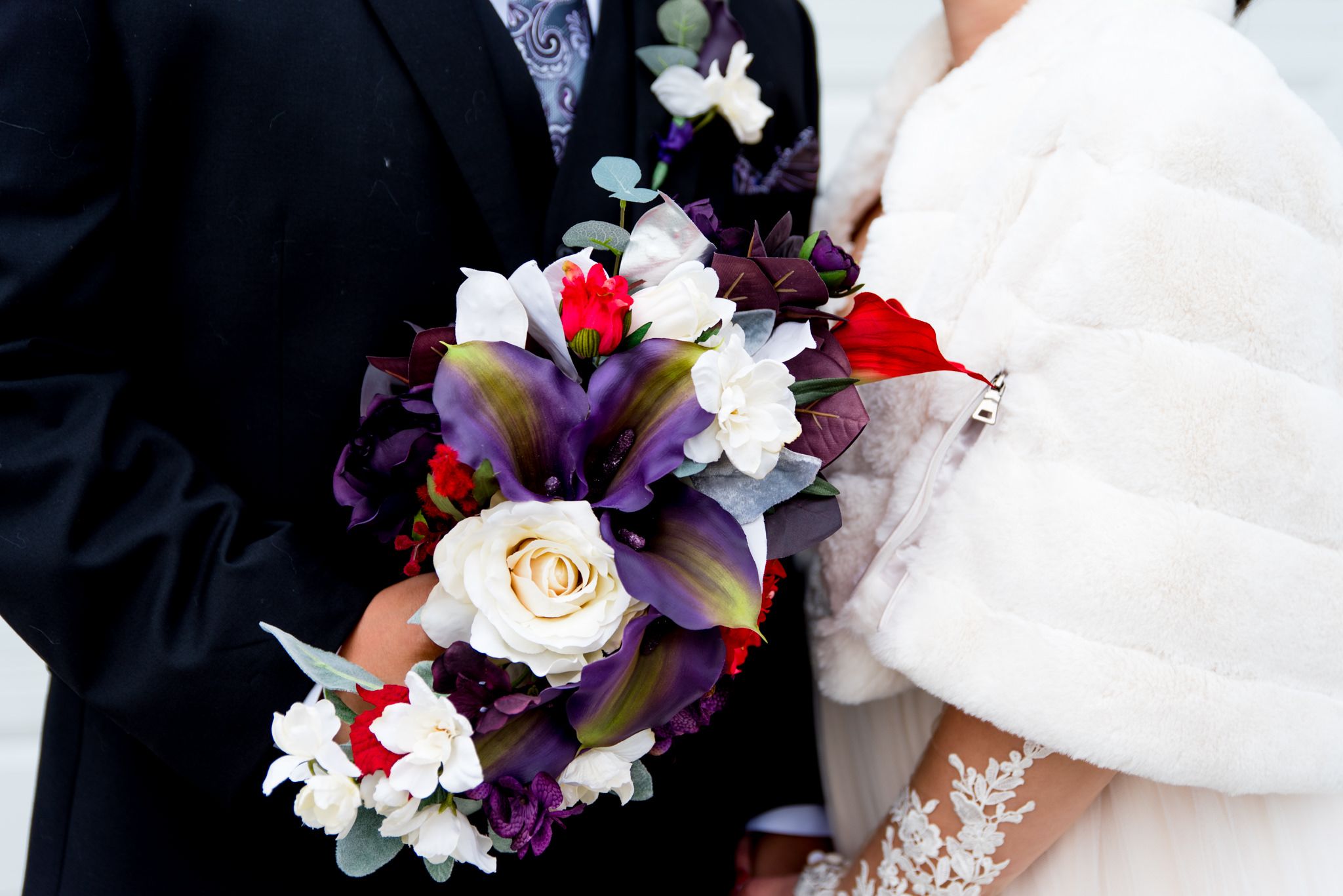 close up of red and purple wedding bouquet with bride and groom holding it