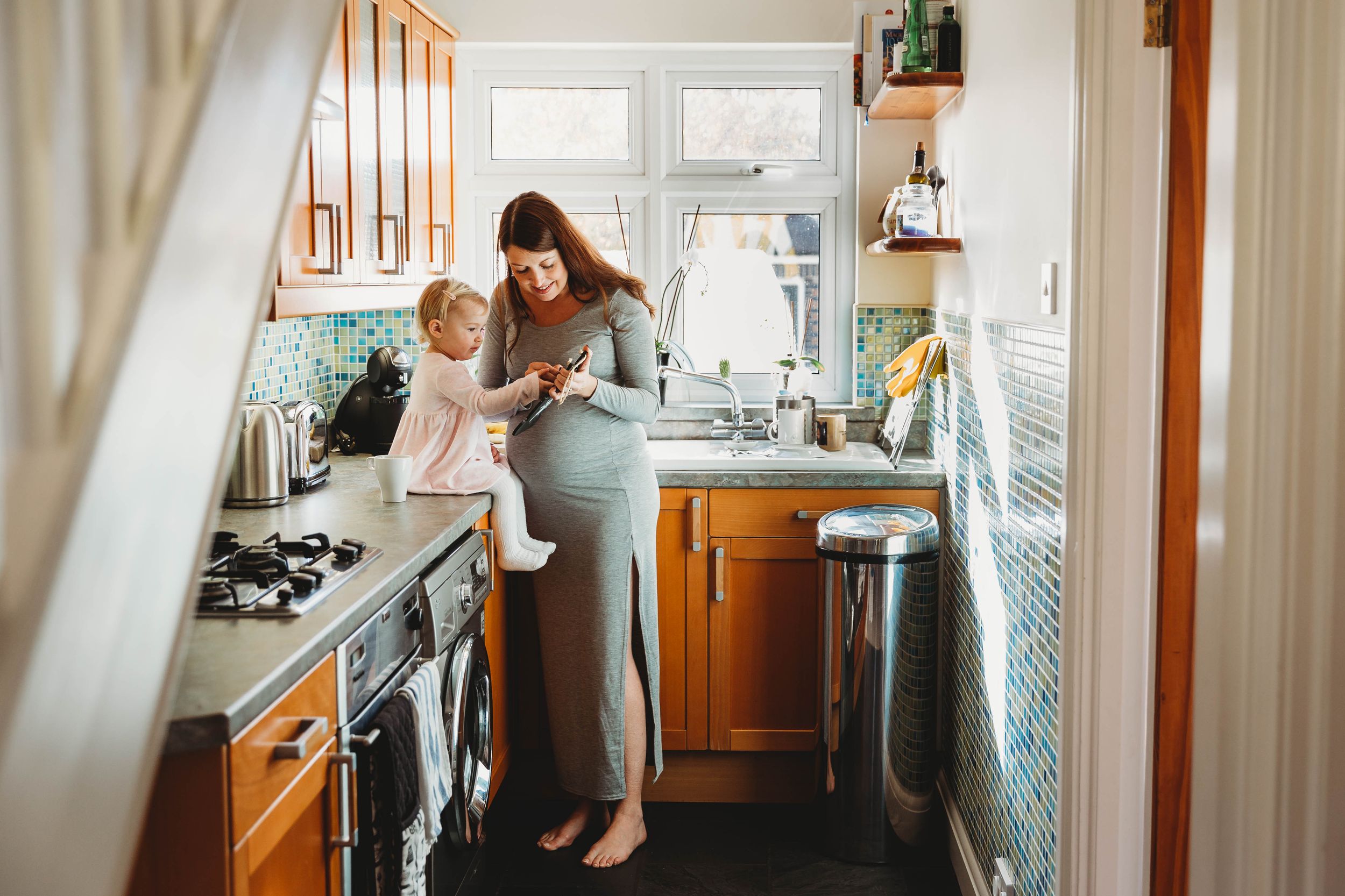 pregnant woman in grey maternity dress standing in kitchen with little girl