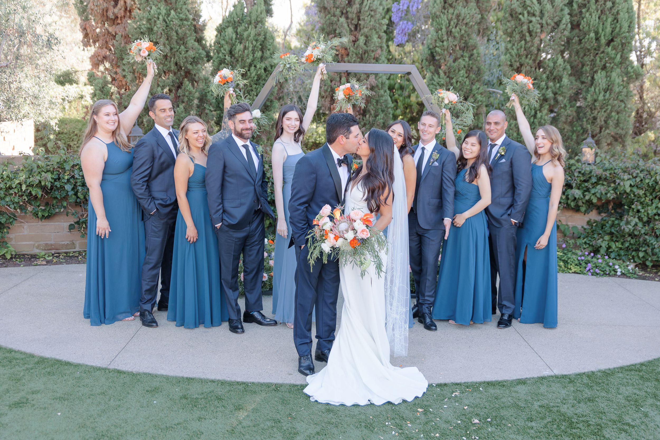 Bride and groom kissing outdoors with bridal party cheering
