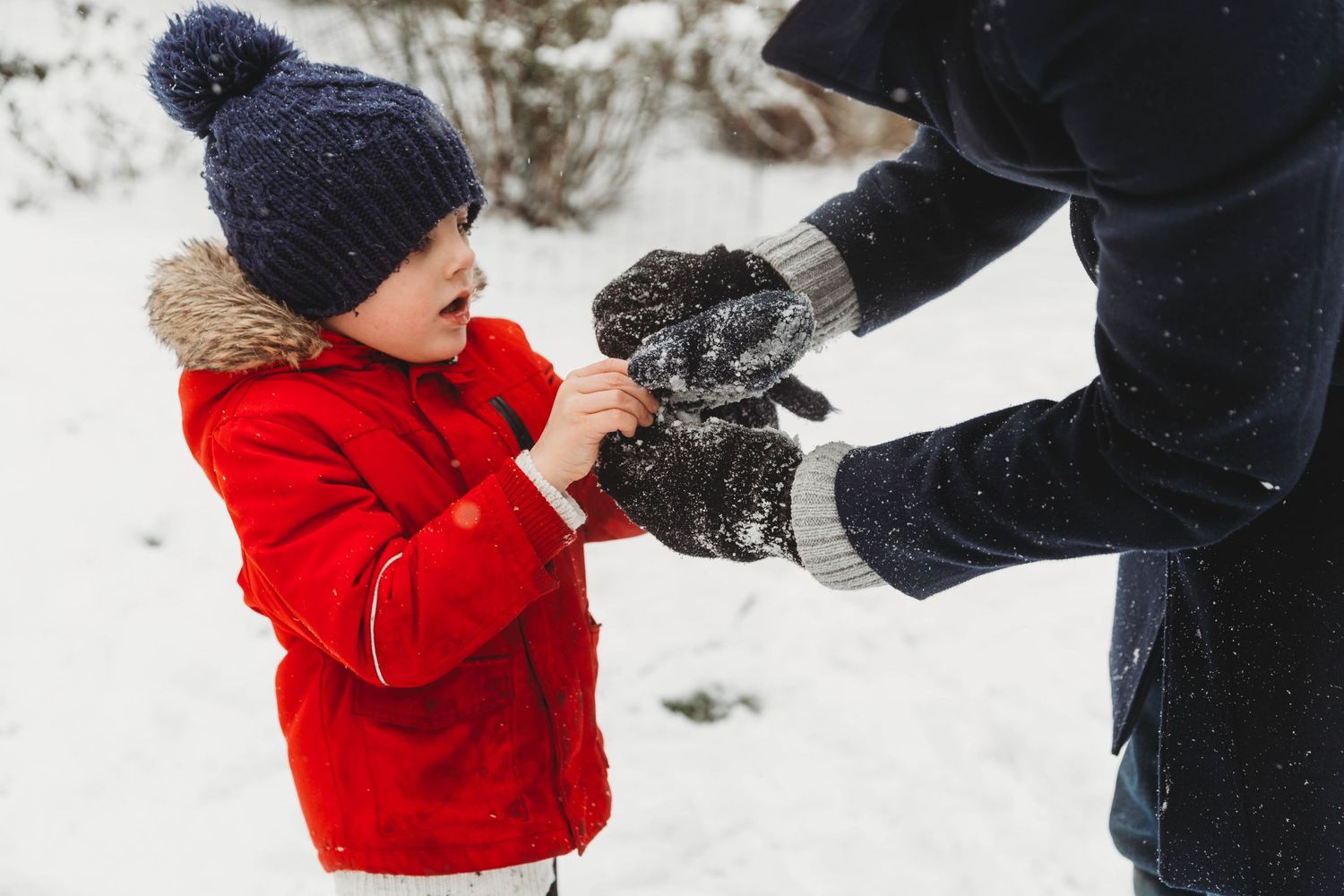 boy in red jacket getting help putting gloves on