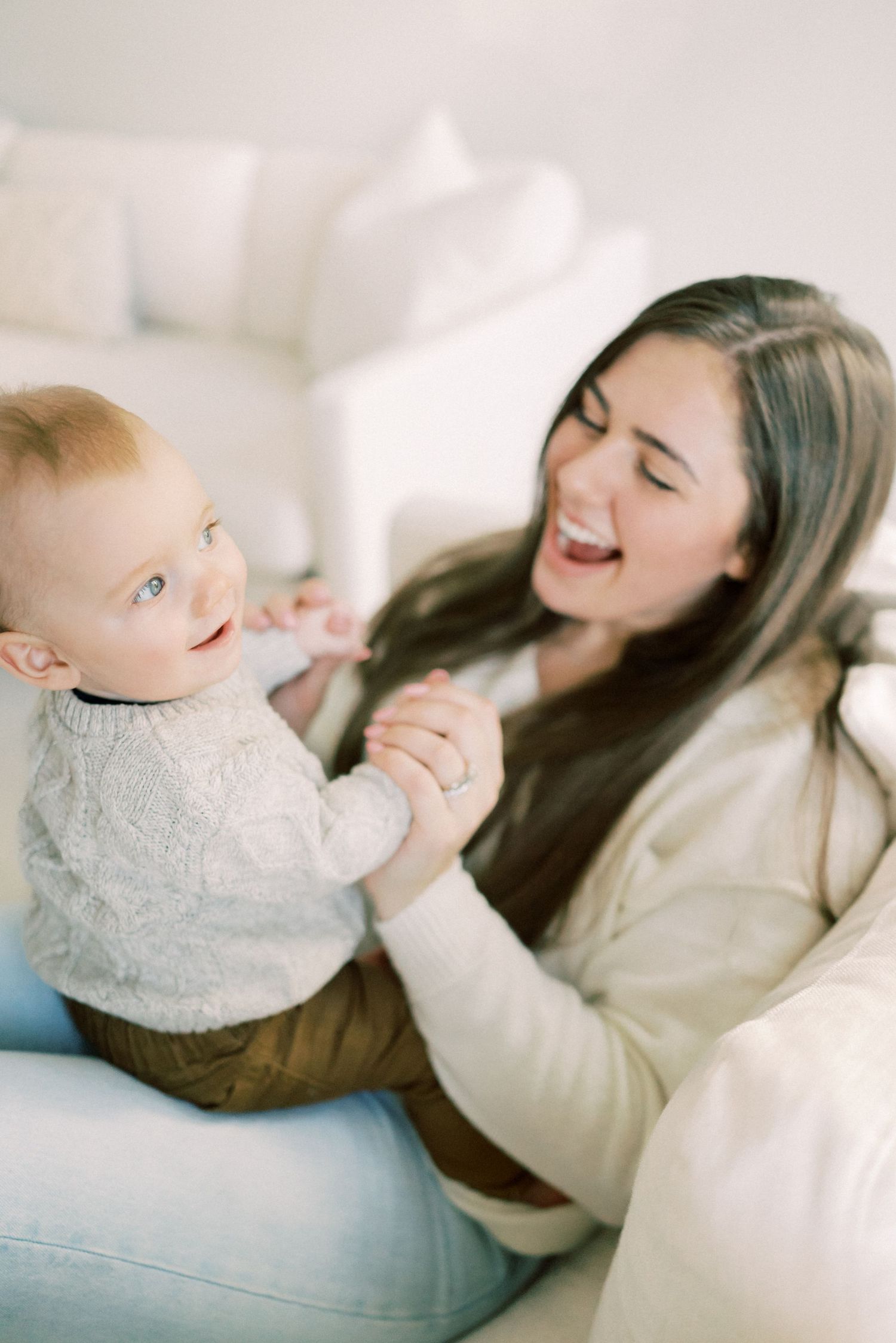 Joyful playtime moment between parent and baby on white couch.