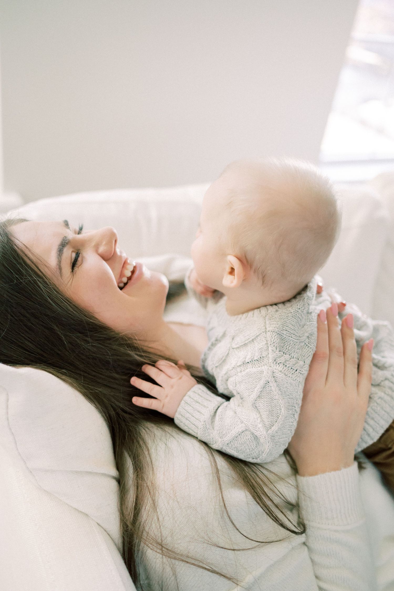 Candid moment of parent and baby laughing together on white couch.