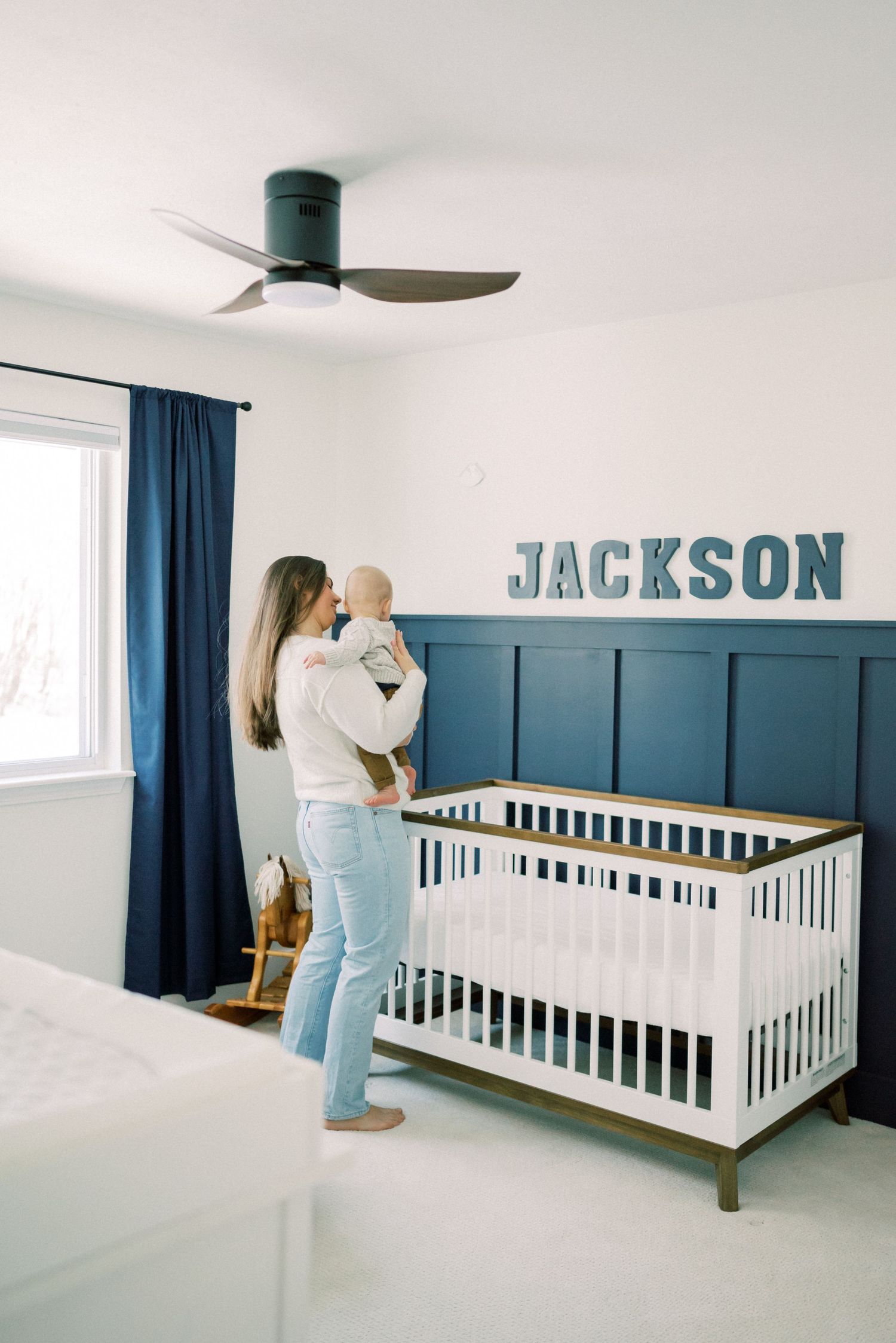 A bright nursery room featuring navy blue wainscoting and matching curtains with decorative wall letters.