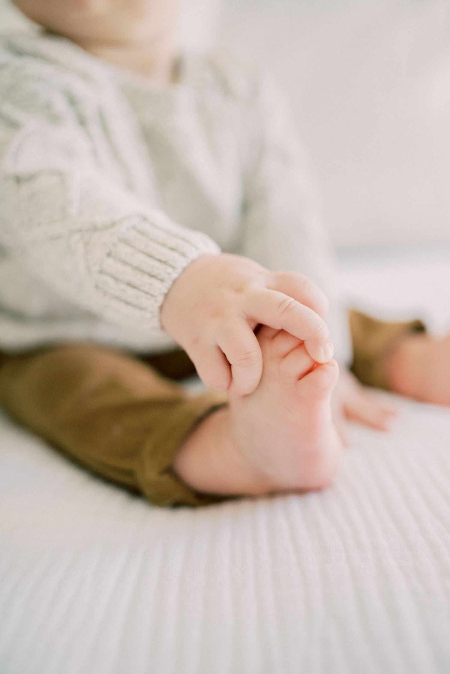 Close up of tiny baby hands grasping soft knit fabric on white bedding.