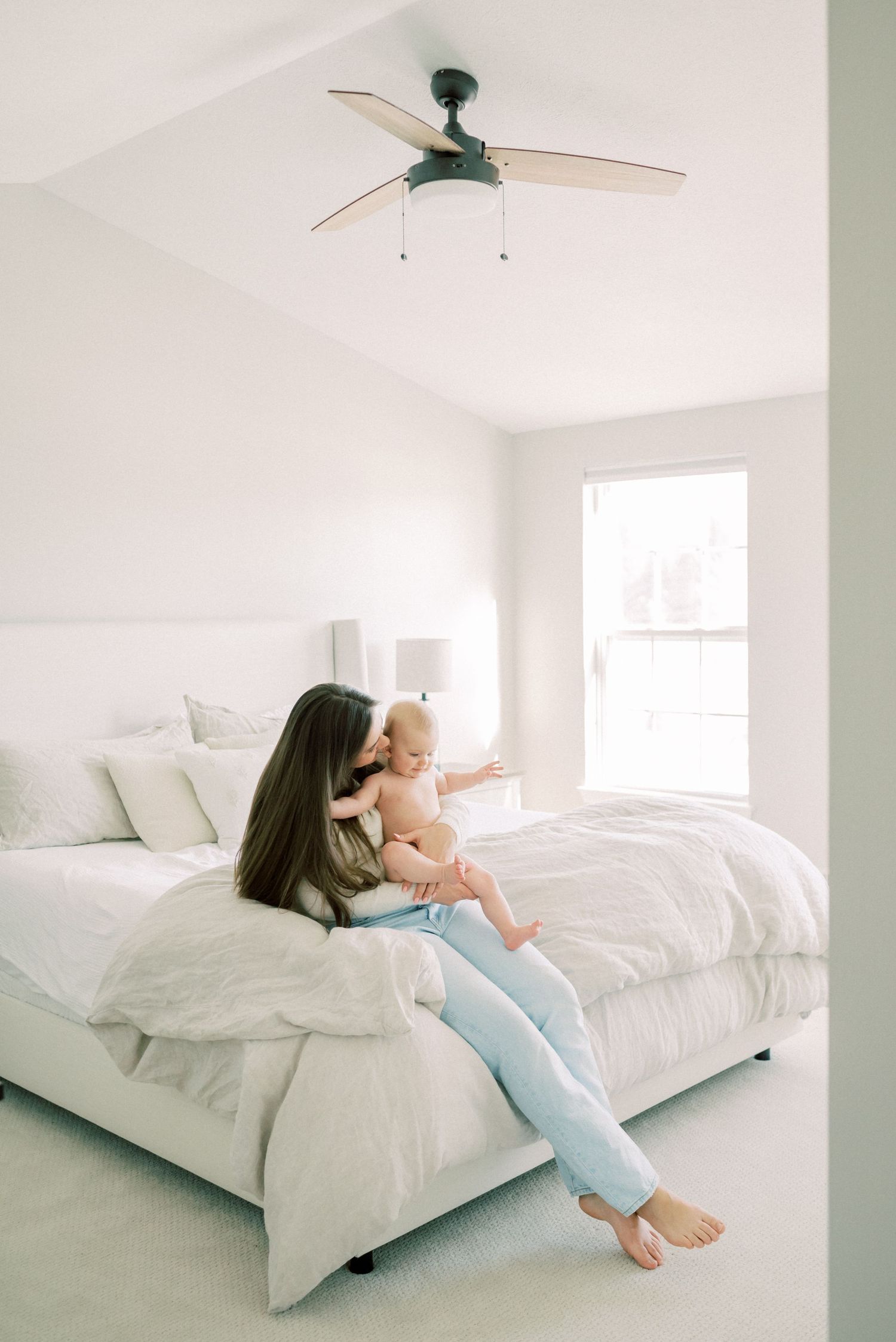 A bright bedroom interior with white bedding and a modern ceiling fan.