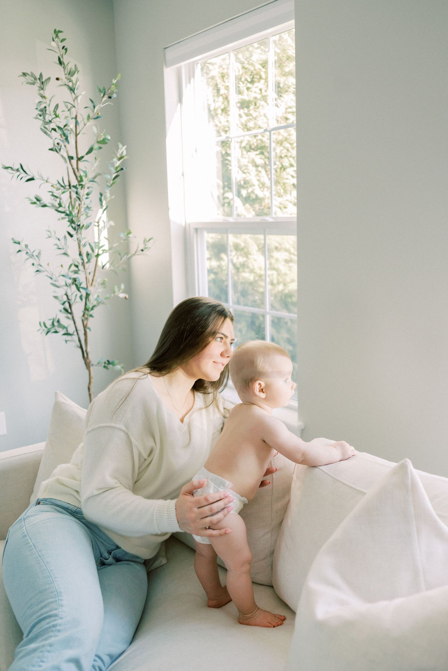 A tender moment by a bright window with a white sofa and decorative plant in a serene living room.