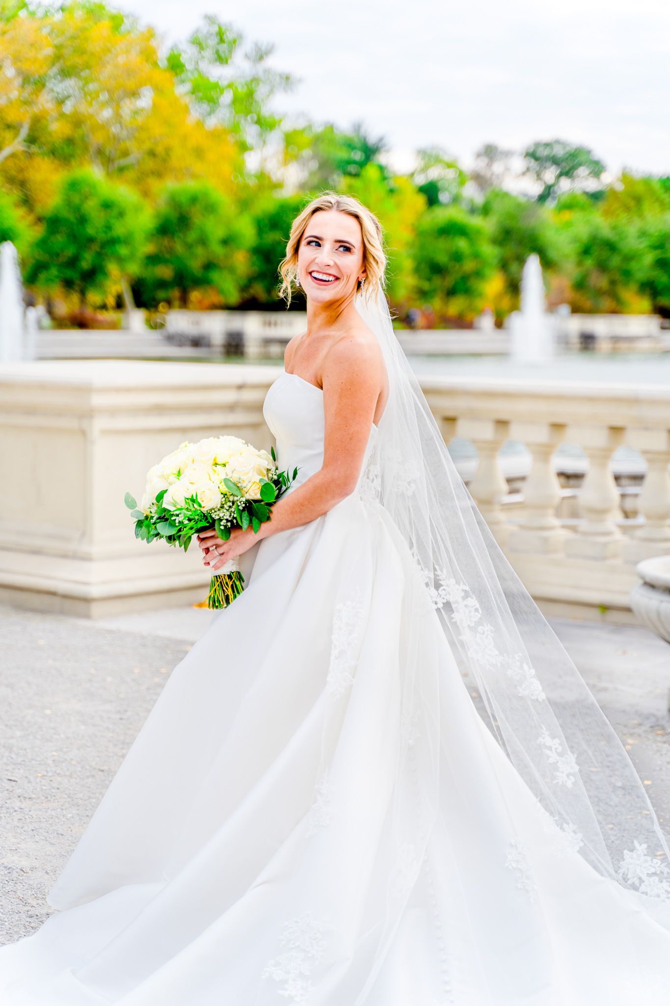 blonde bride with updo and long veil and white bouquet looking over her shoulder in Forest Park wedding pictures
