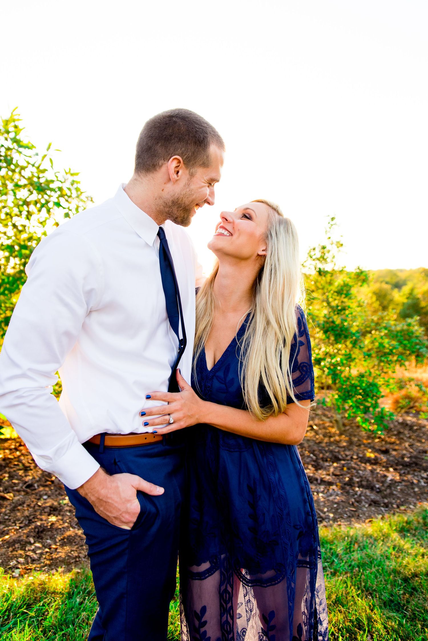 woman with long blonde hair in navy dress smiles at husband in white shirt and navy pants and tie