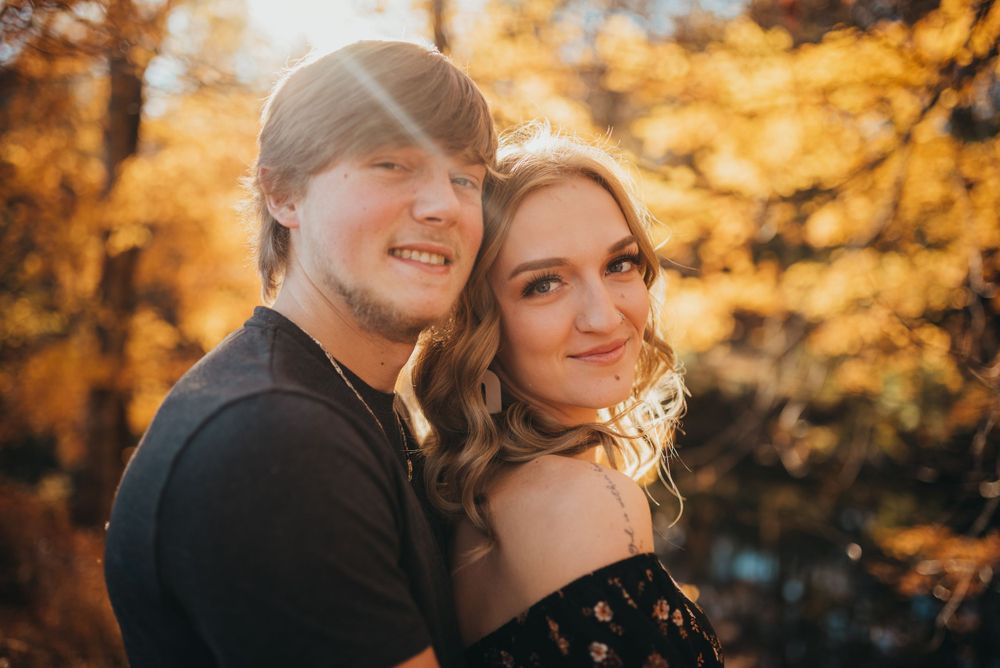 Couple posing together against vibrant autumn foliage at sunset.