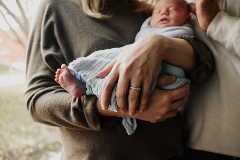 Vanourny Newborn Session Lifestyle Kansas City Photography Mom holding loosely swaddled newborn with baby foot dangling