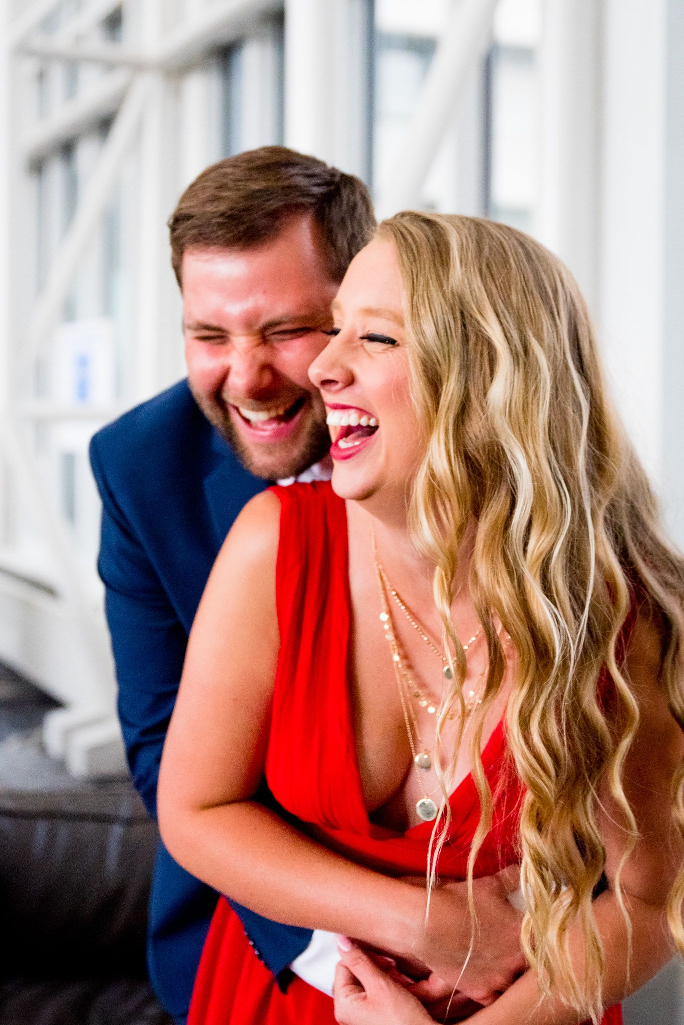 blonde woman in red dress laughing with fiance in navy suit at Galt House Hotel engagement pictures