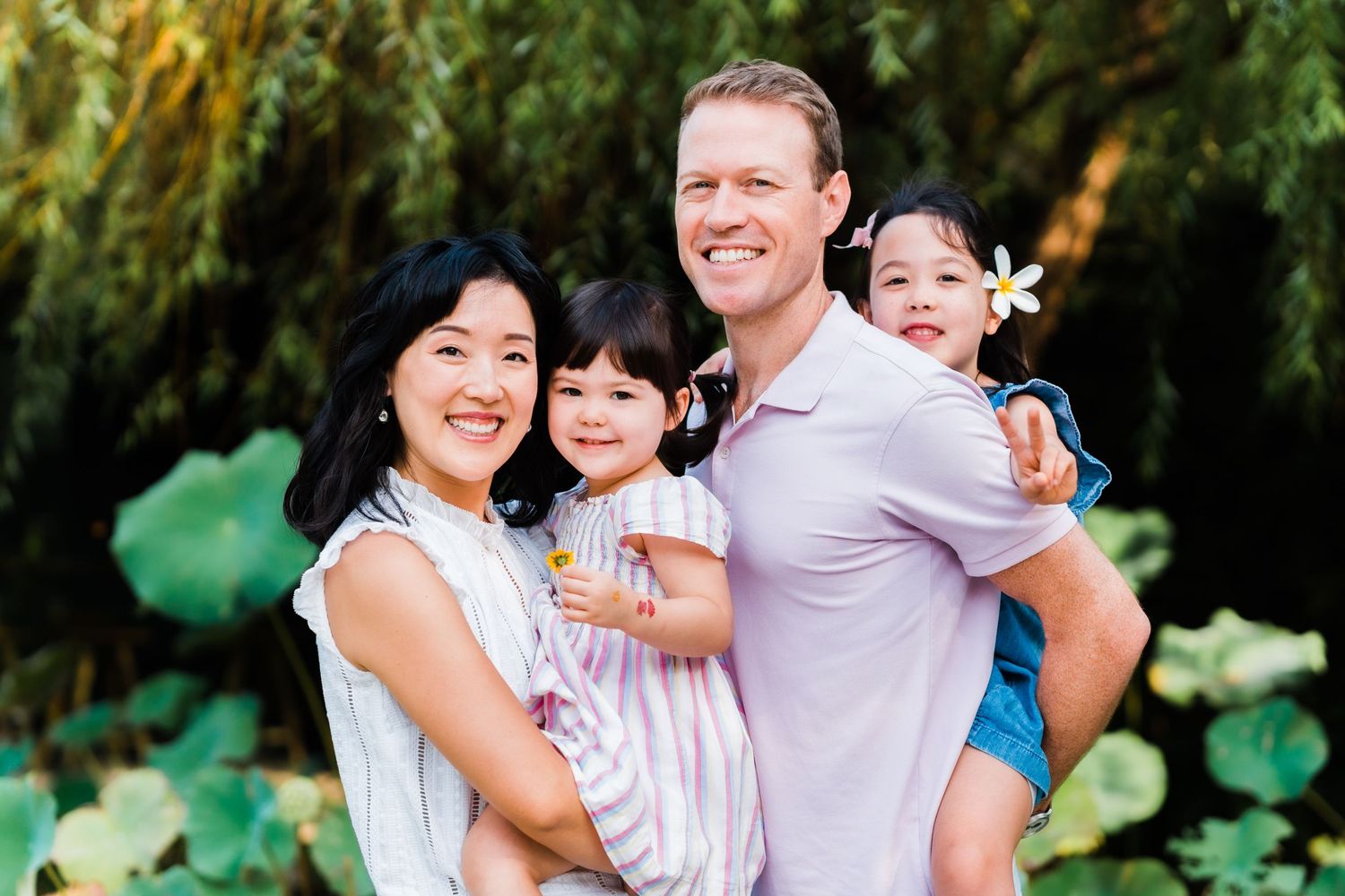 Joyful family portrait in a lush garden setting with green foliage backdrop.