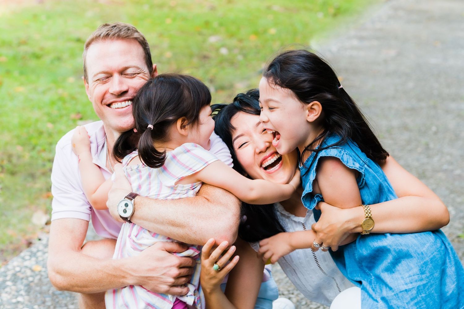 Candid family moment of laughter and hugs on grassy pathway.