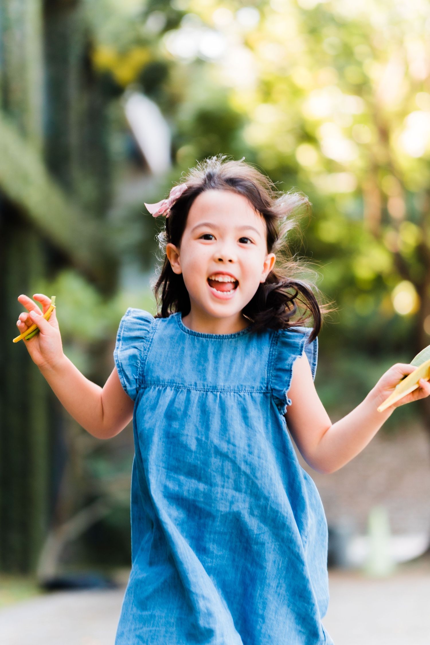 Energetic child in blue dress jumping and playing outdoors with natural backdrop.
