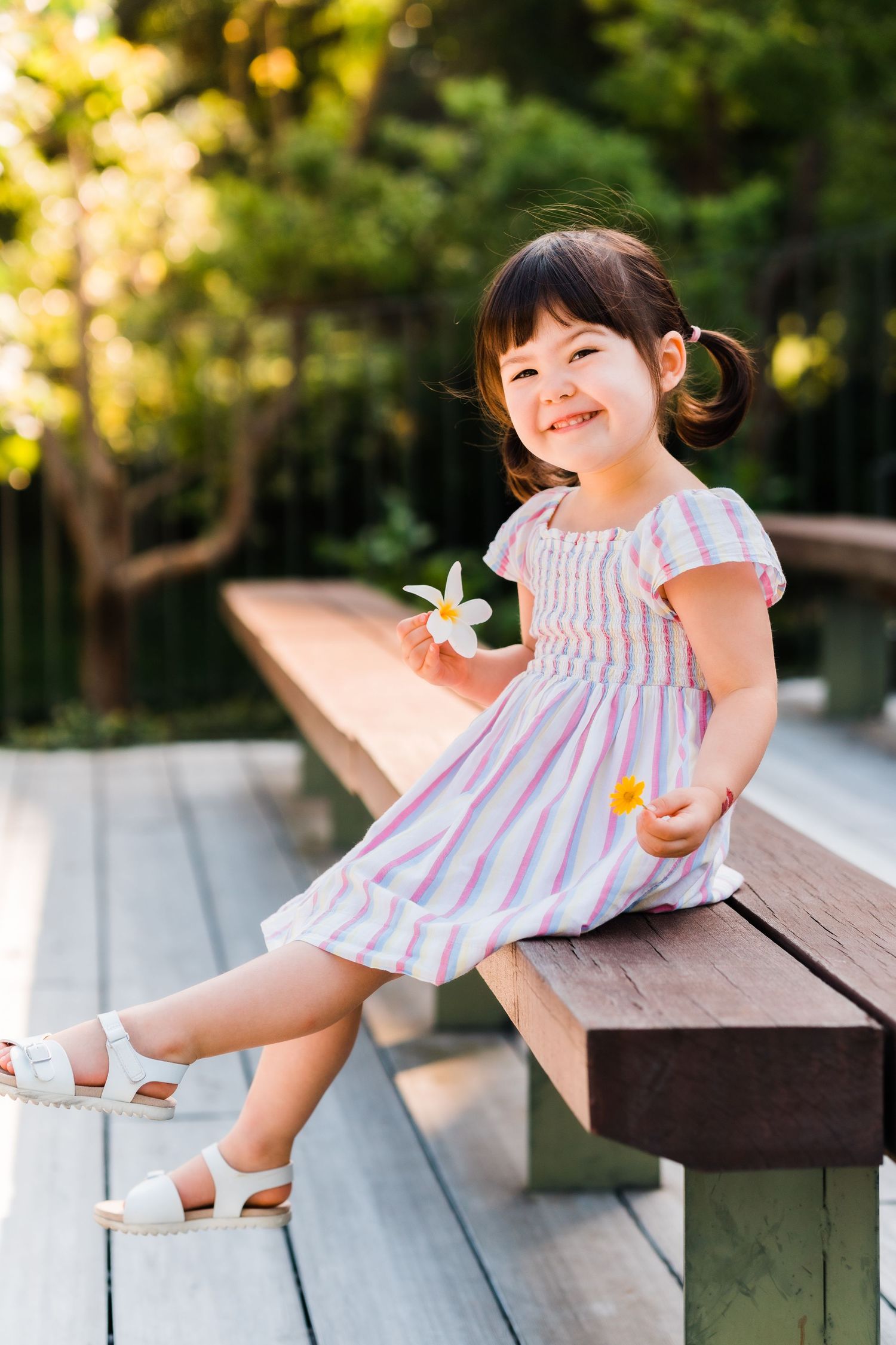 toddler holds orchid flower and smiles while sitting on a brown bench