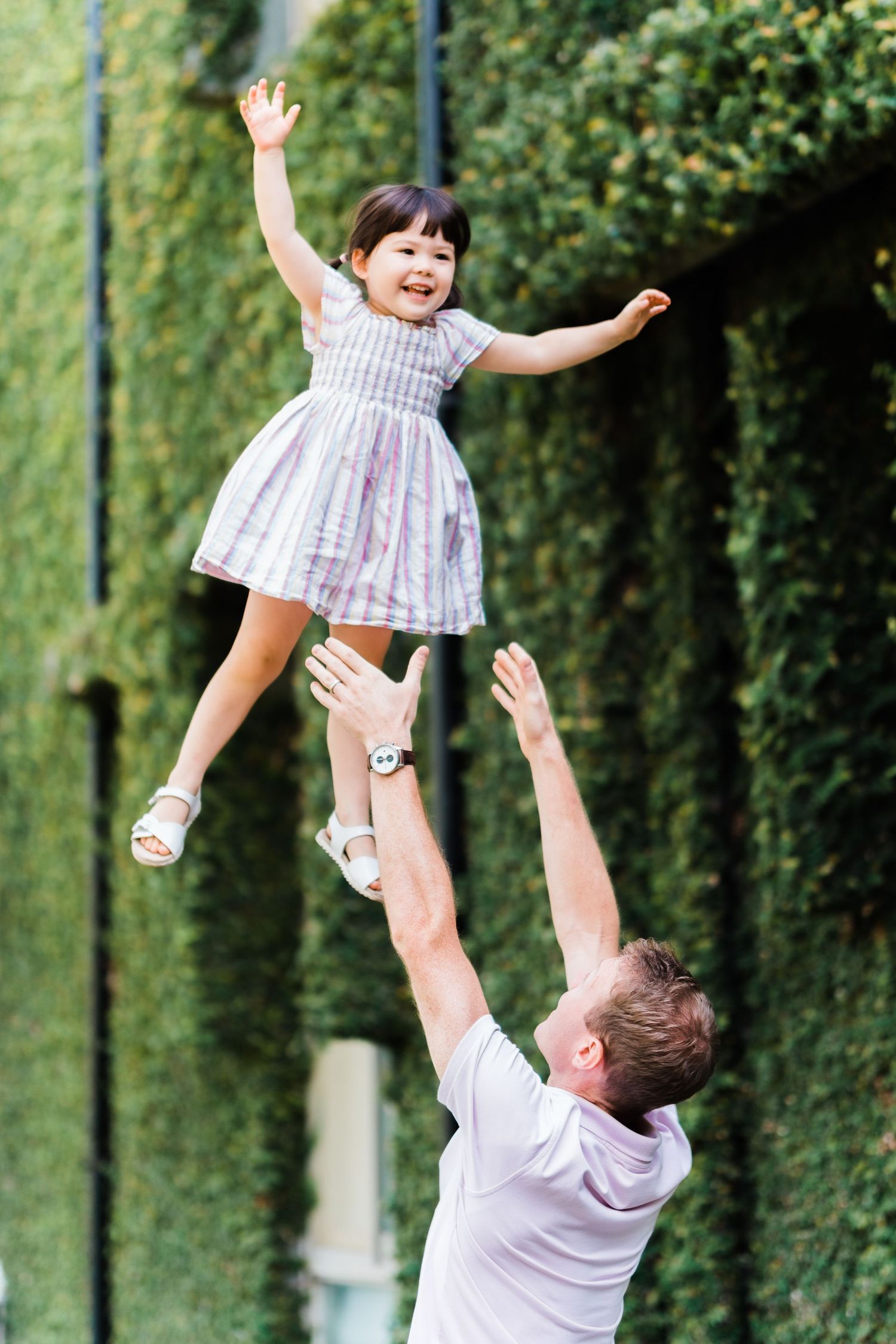 dad throws daughter into the air and daughter smiles and holds her arms out