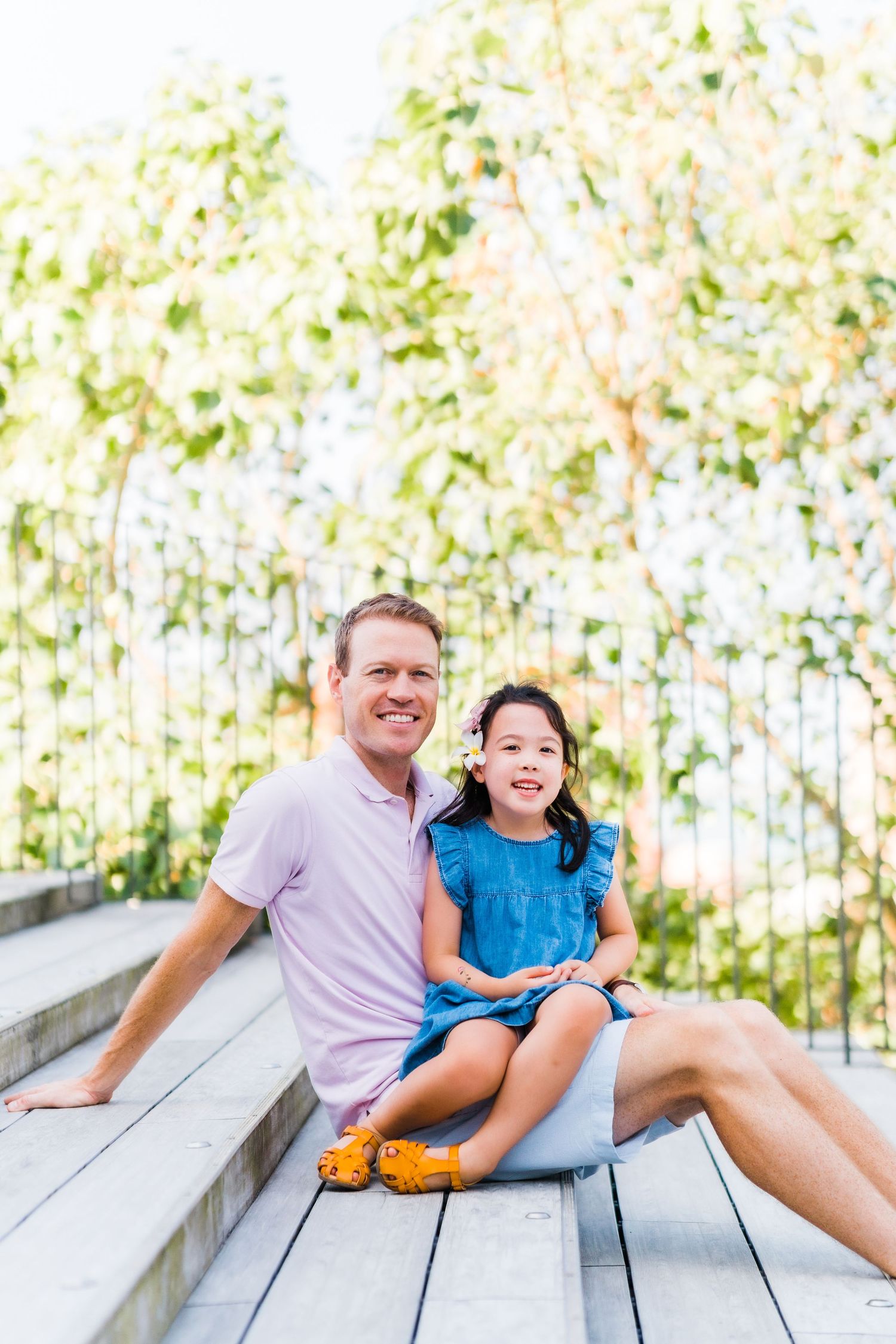Parent and child sitting together on wooden bench stairs in a sunny garden.