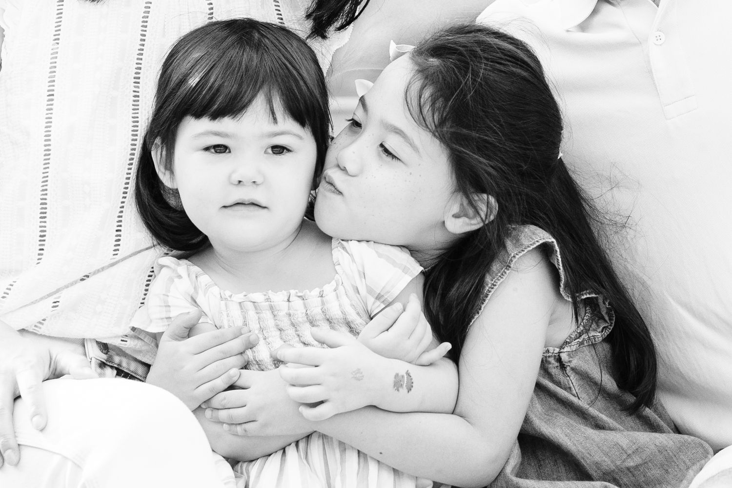 older sister kisses younger sister while she frowns