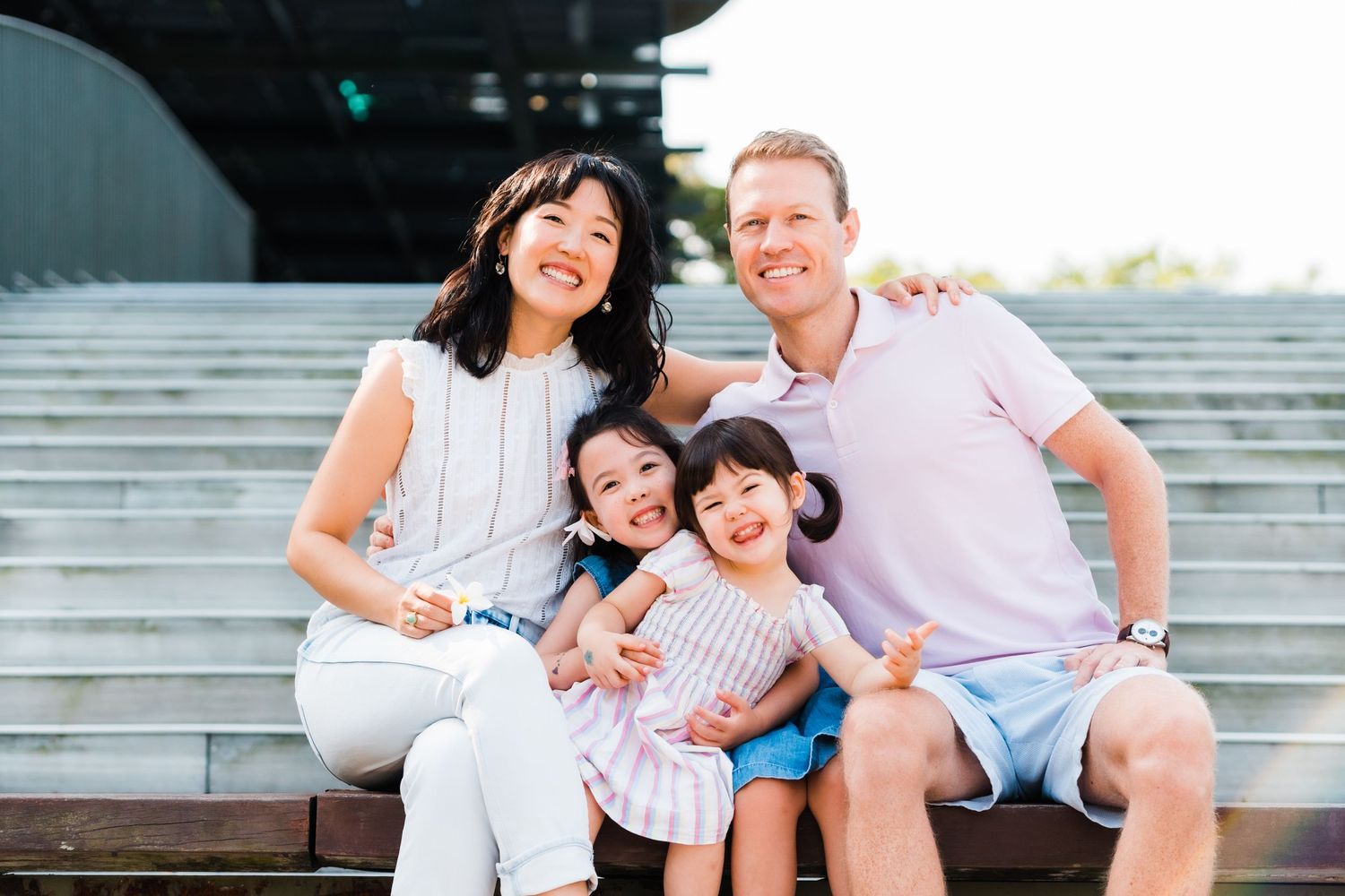 a sweet family portrait where everyone is looking and smiling while sitting on a brown bench