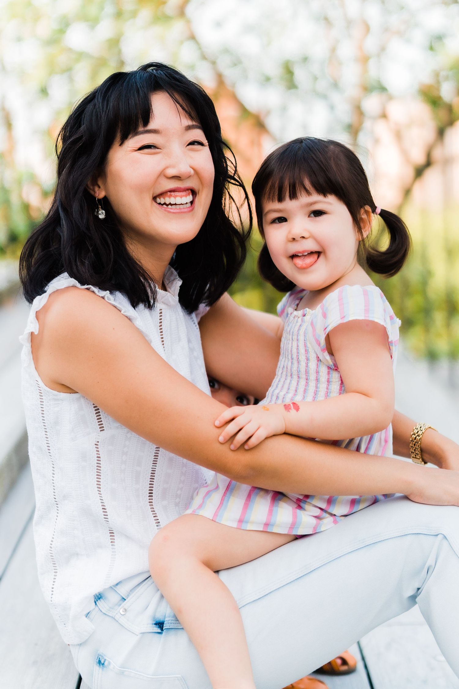 daughter sticks tongue out at camera while sitting on mom's lap