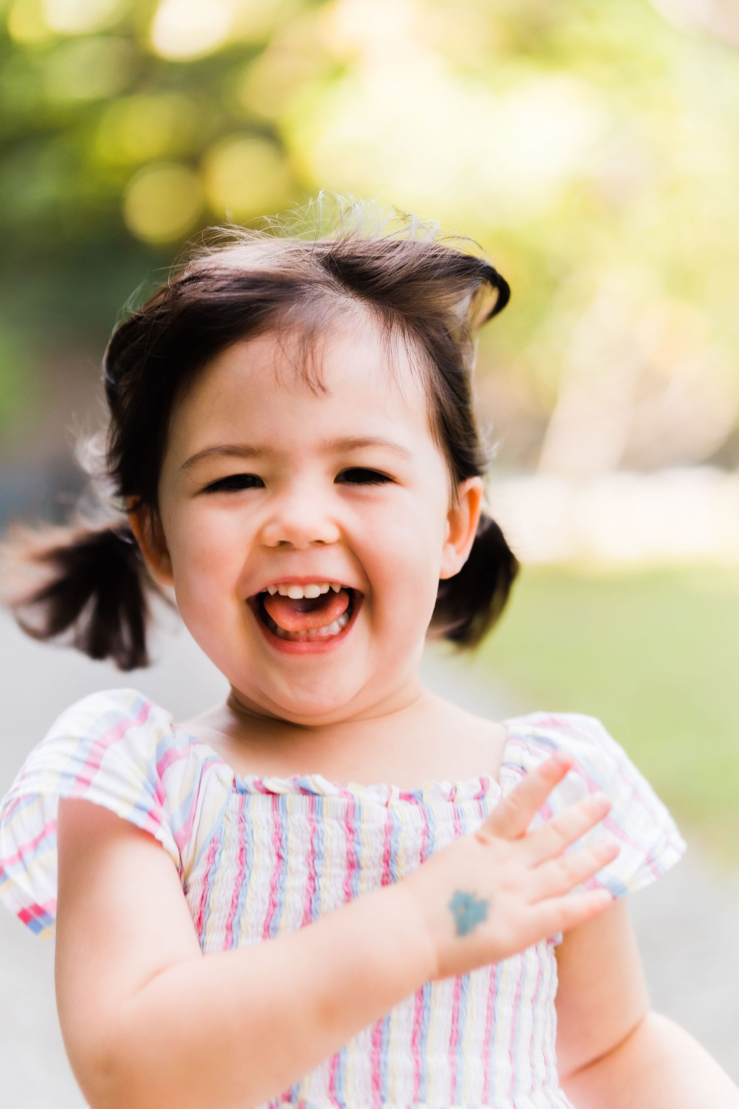 Joyful child laughing with pigtails wearing striped dress outdoors.