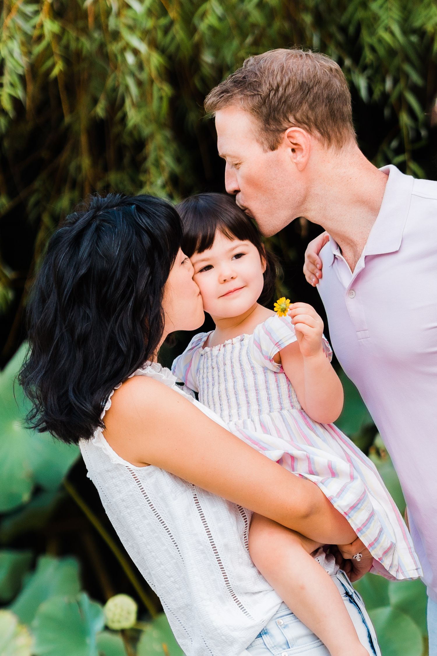 parents kiss youngest daughter while she holds a lily flower in taiwan