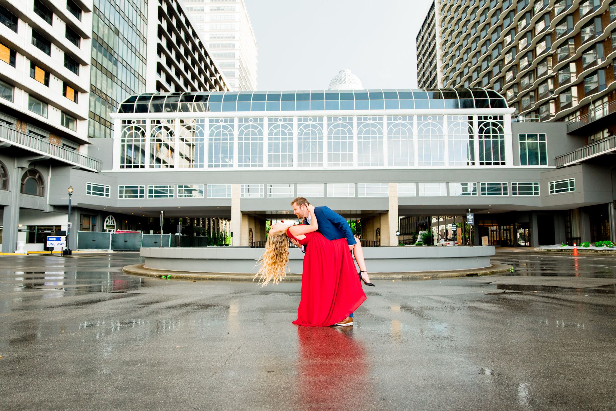 man in navy suit dipping woman in red dress with blonde hair and she laughs