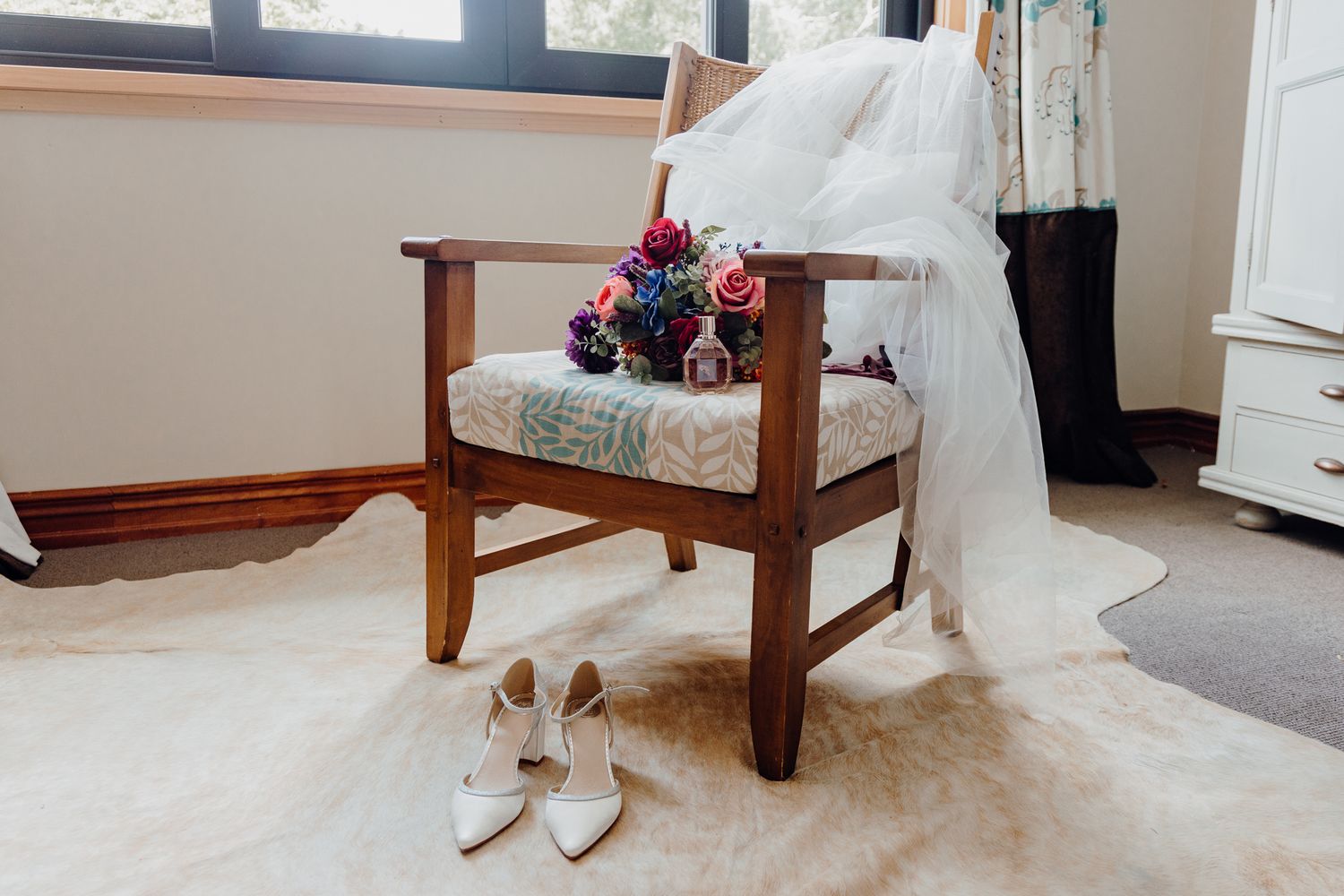 Wedding dress draped over wooden chair with bridal shoes placed underneath.