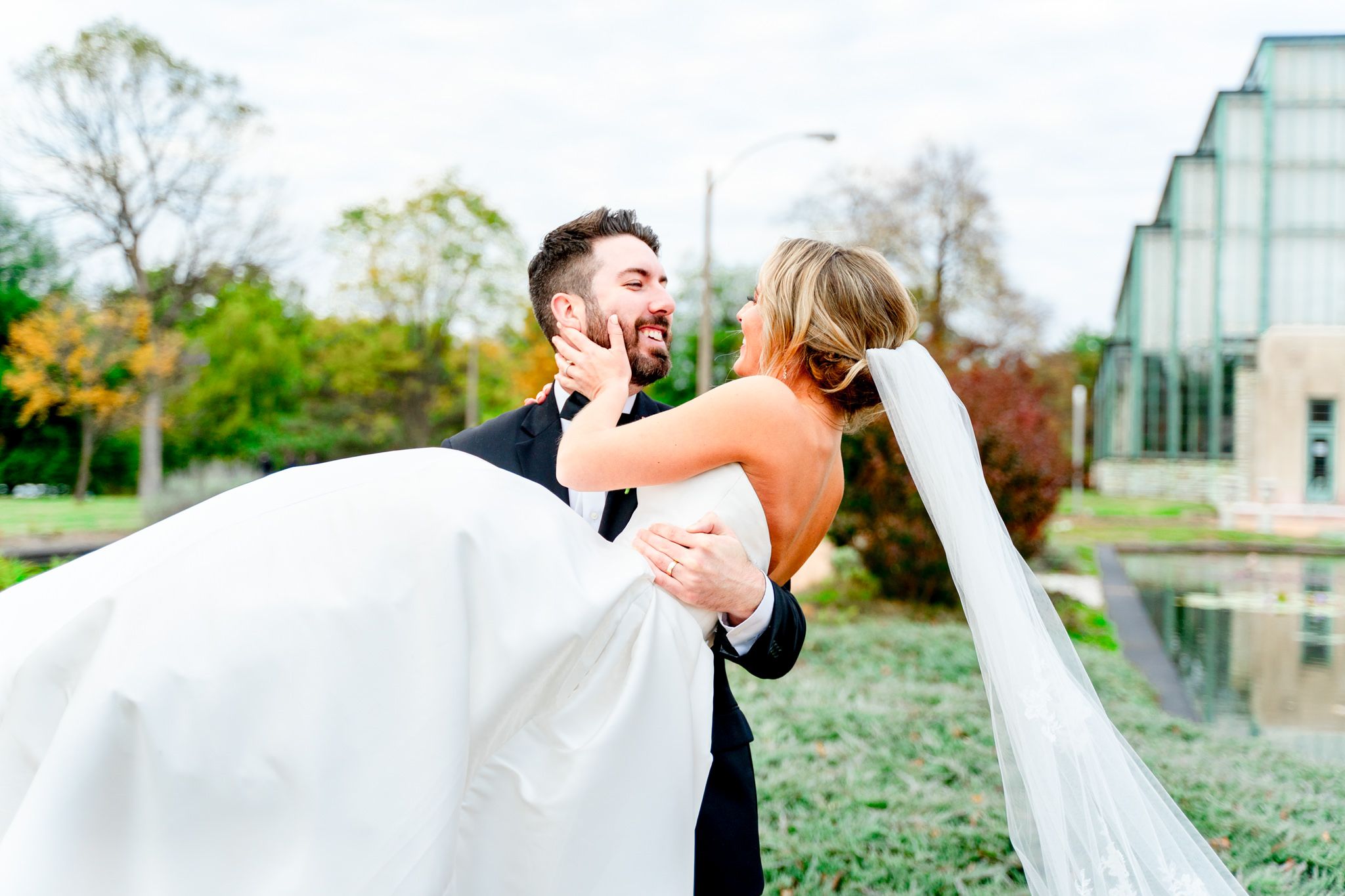 groom carrying bride in his arms and smiling at each other at the Jewel Box in Forest Park, STL