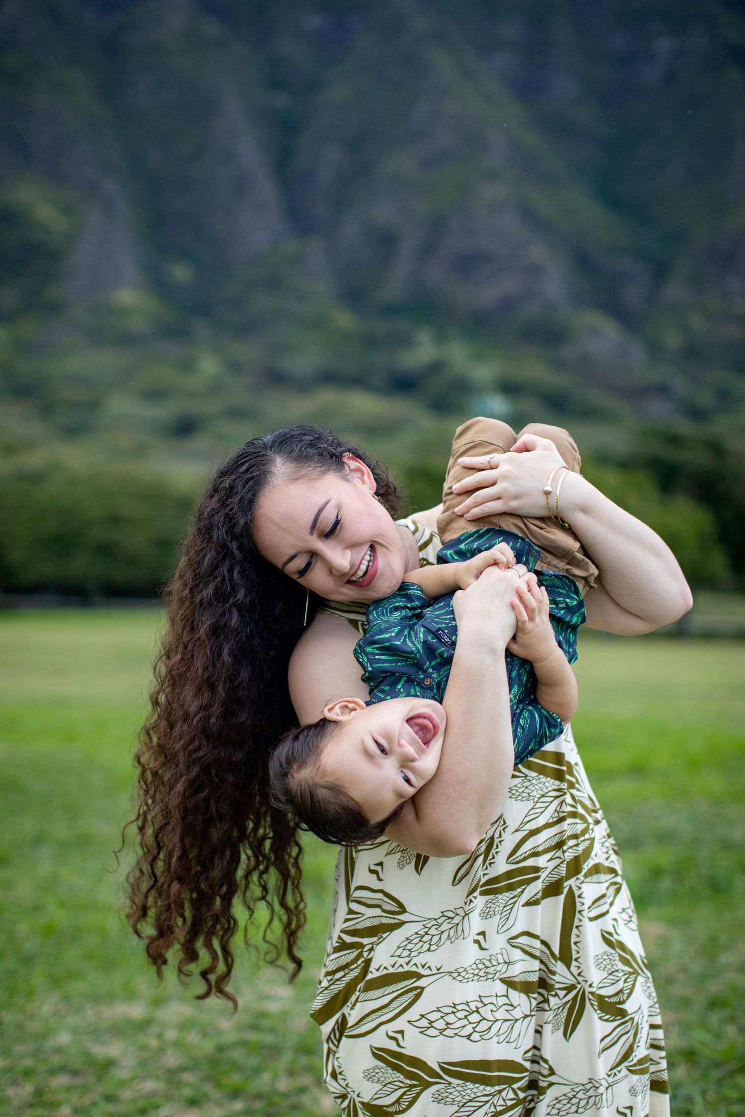 Playful moment between parent and child in tropical Hawaiian setting with mountains.