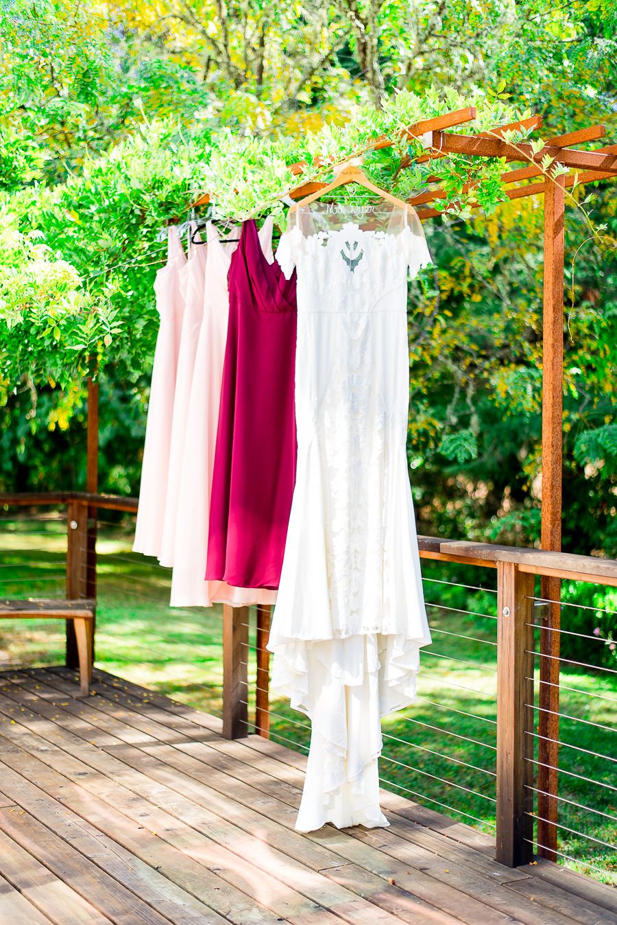 red and blush bridesmaids dresses and wedding dress hanging side by side for Northern California Vineyard wedding