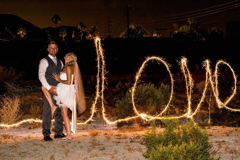 Couple standing in front of 'LOVE' written in sparklers at night.