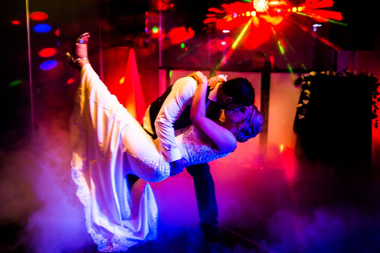 Dramatic dip dance pose with flowing white dress in purple and red lighting.