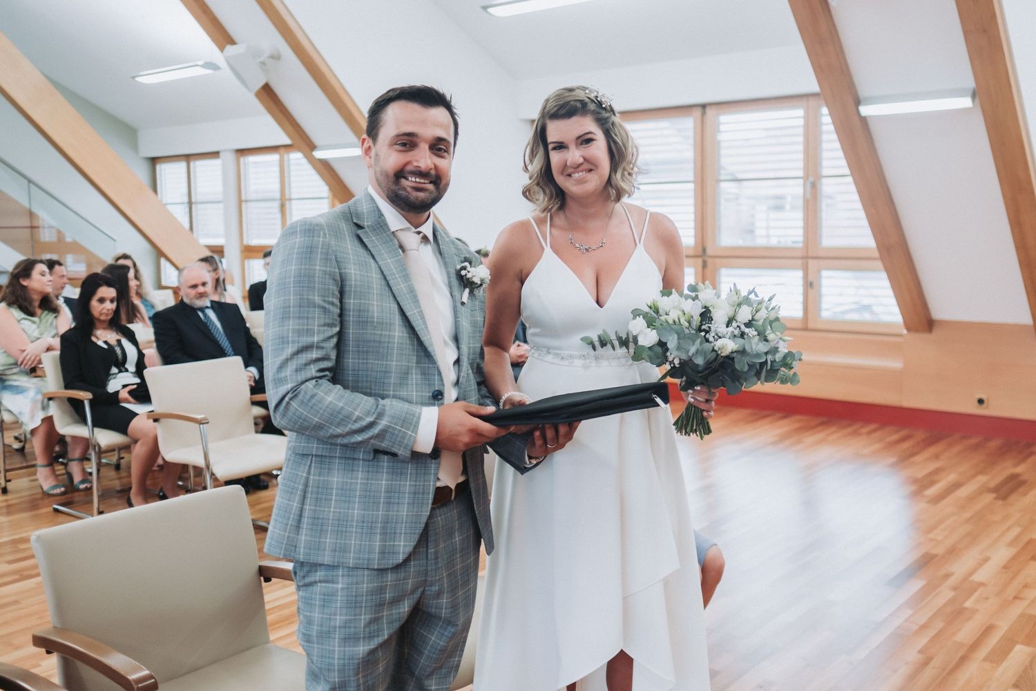 Happy couple sharing joyful moment during indoor wedding ceremony with natural lighting.
