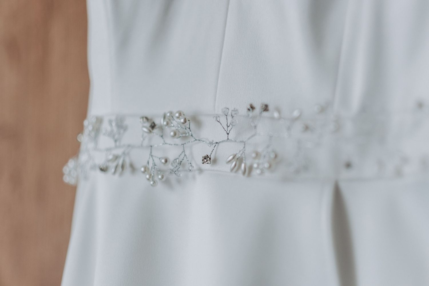 Delicate beaded detail on white wedding dress fabric shown in close-up.