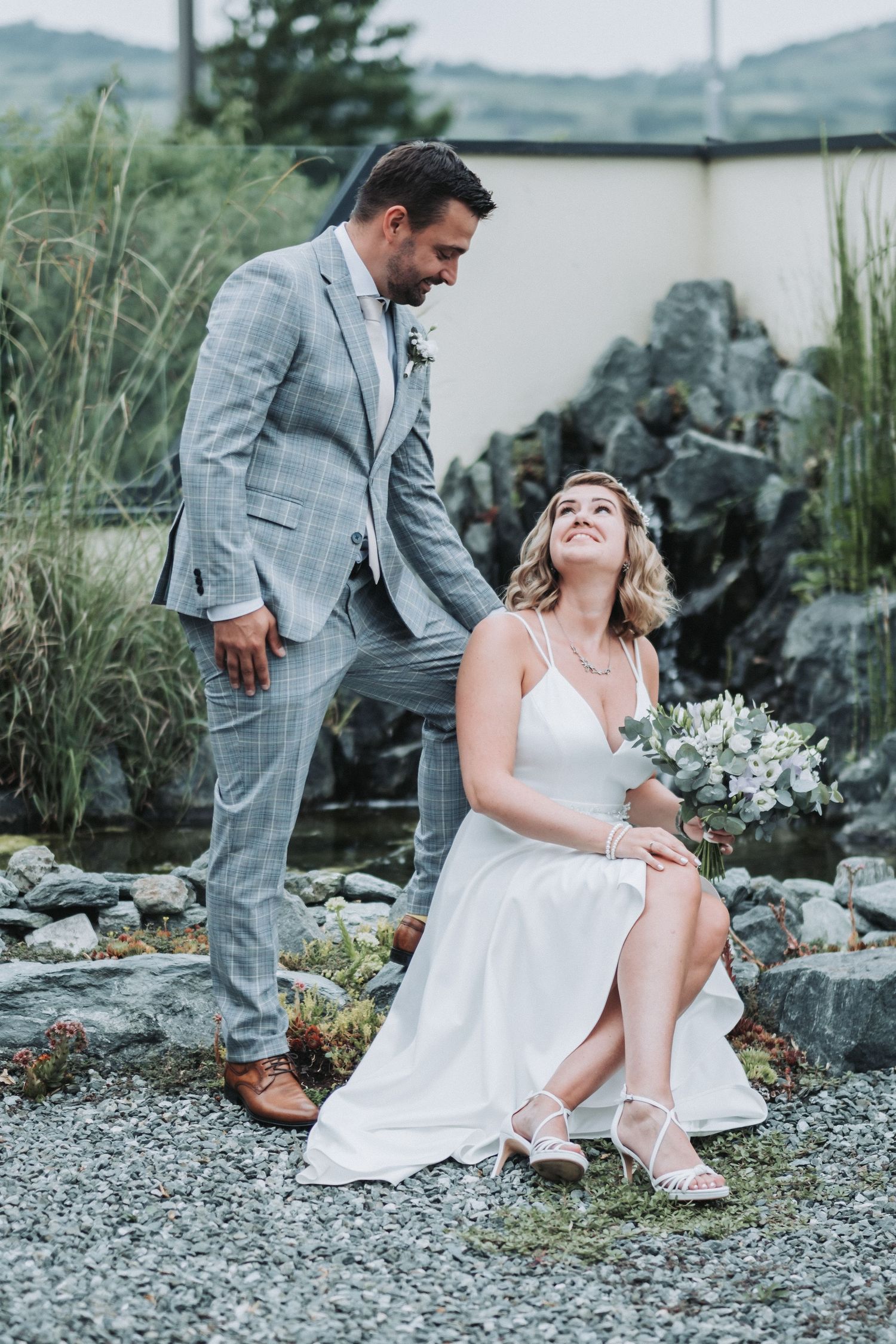 Candid wedding photo of couple laughing together on rocky outdoor terrain.