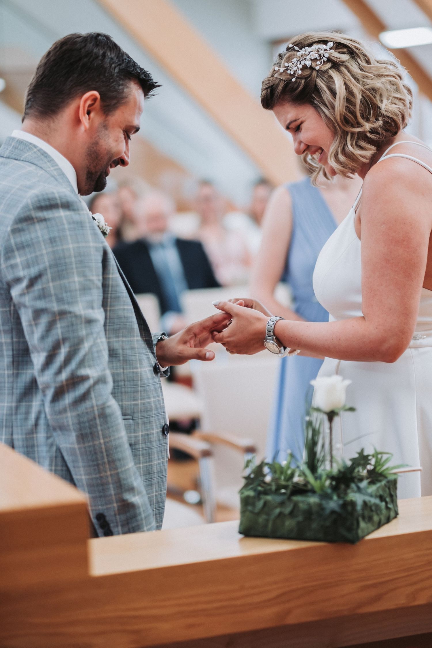Wedding ceremony exchange of rings between couple in grey suit and white dress at modern venue.