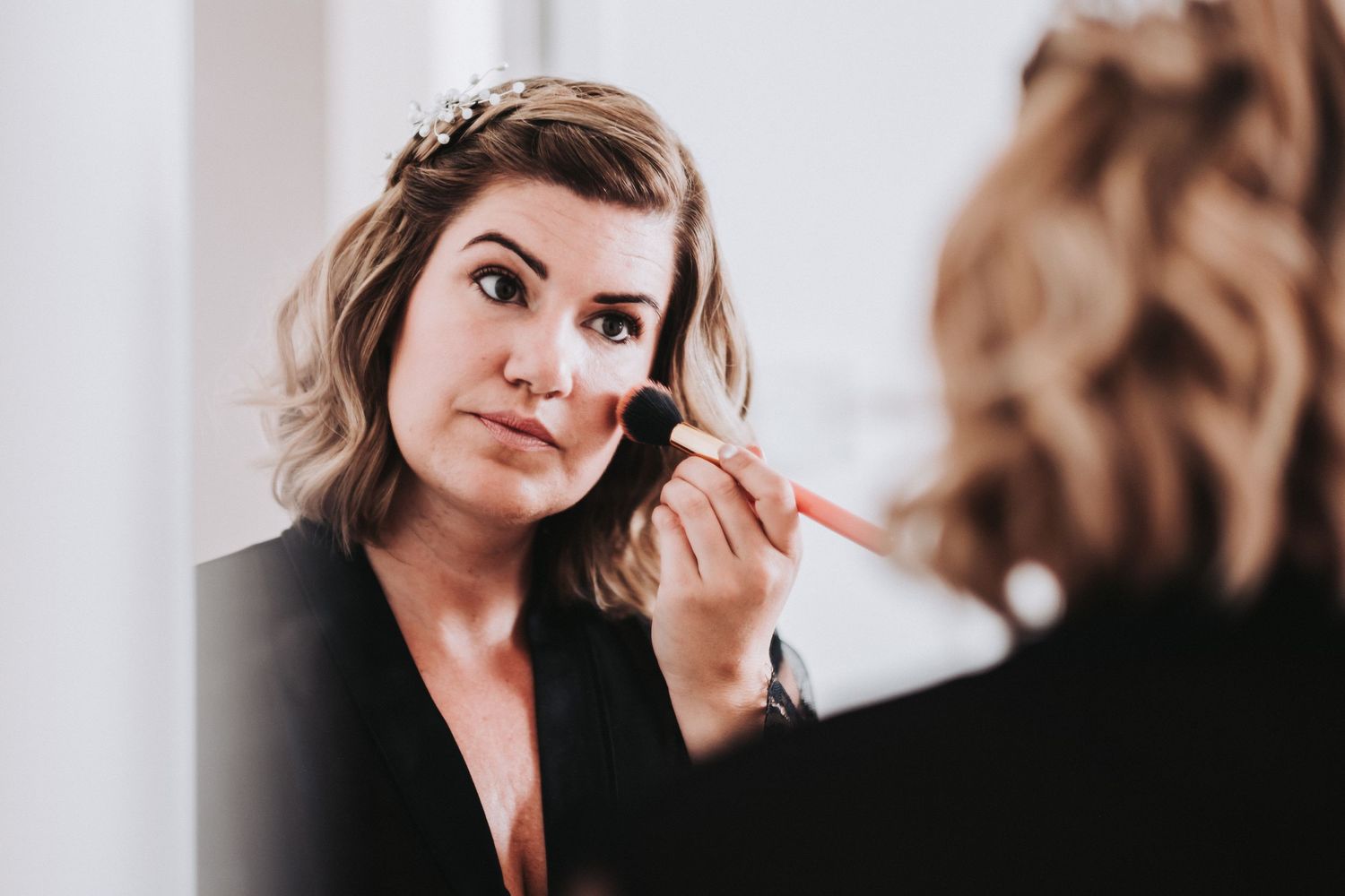 Person applying makeup while looking in mirror during wedding preparation.