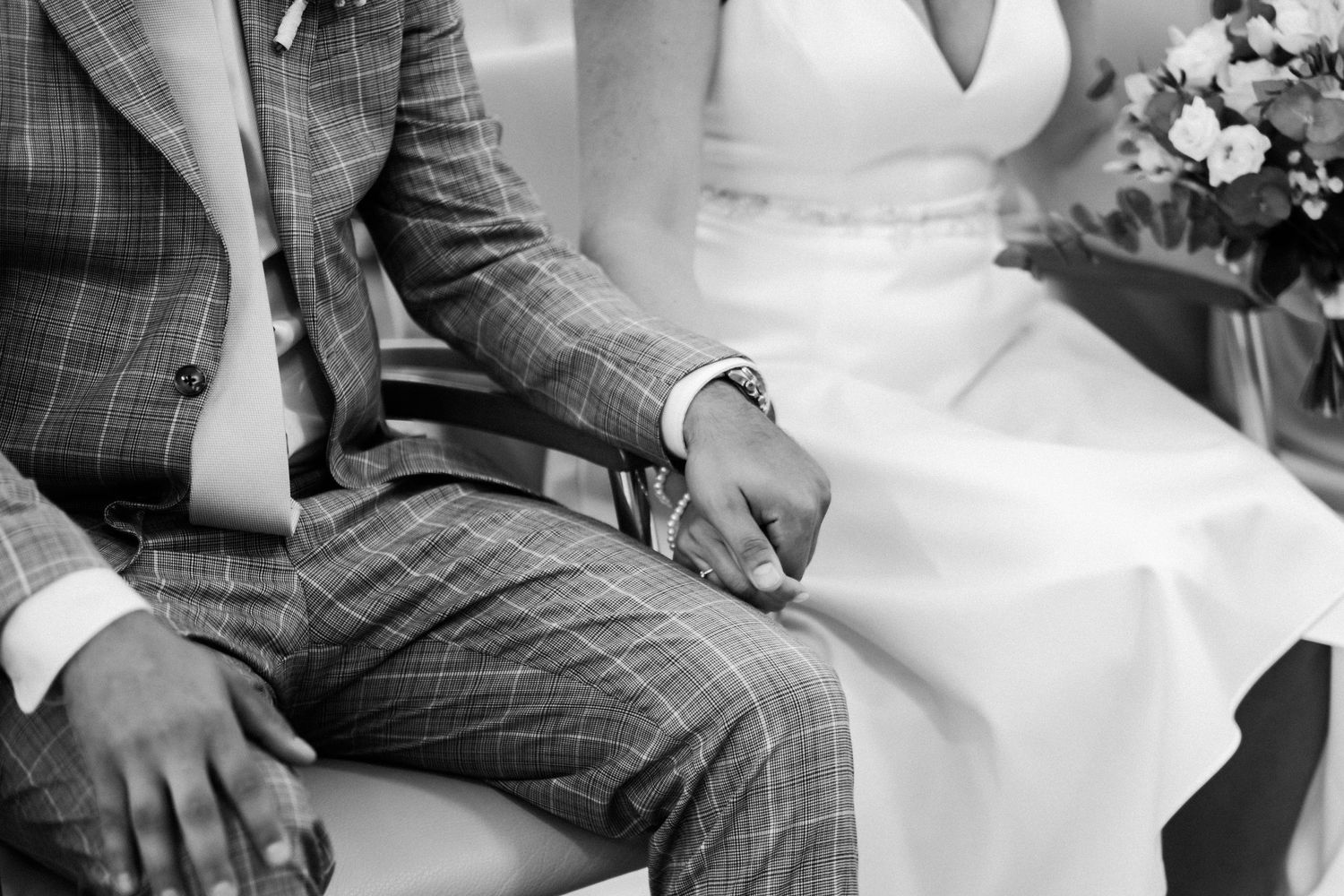 Black and white detail shot of couple sitting together during wedding ceremony.