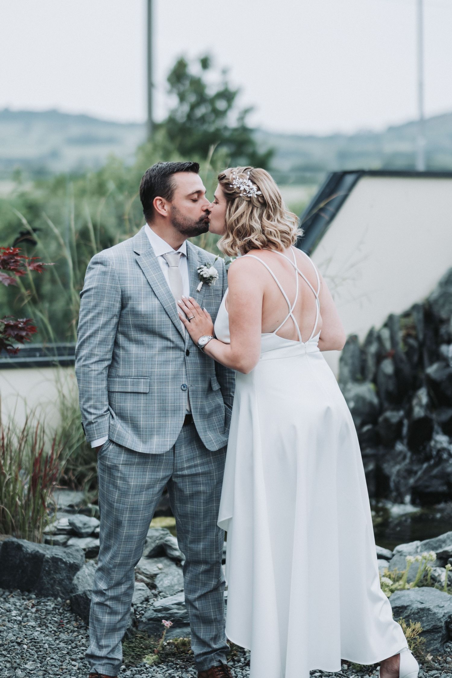 Romantic wedding couple kissing outdoors with mountainous backdrop and natural landscape.