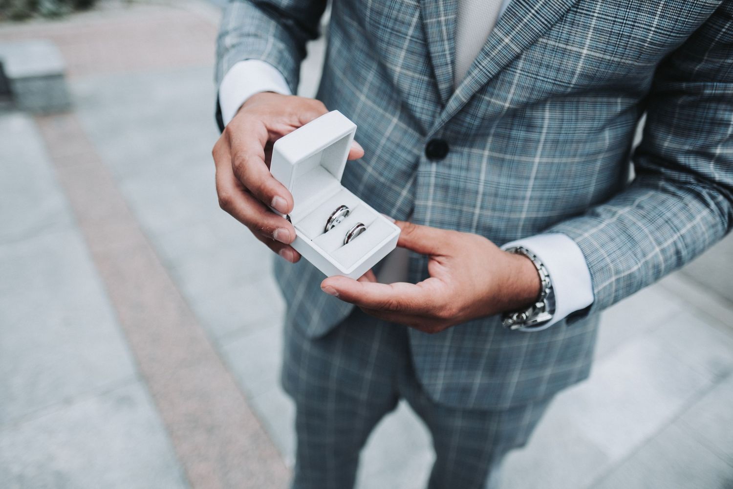 Close up of groom in plaid suit holding open ring box displaying wedding band.