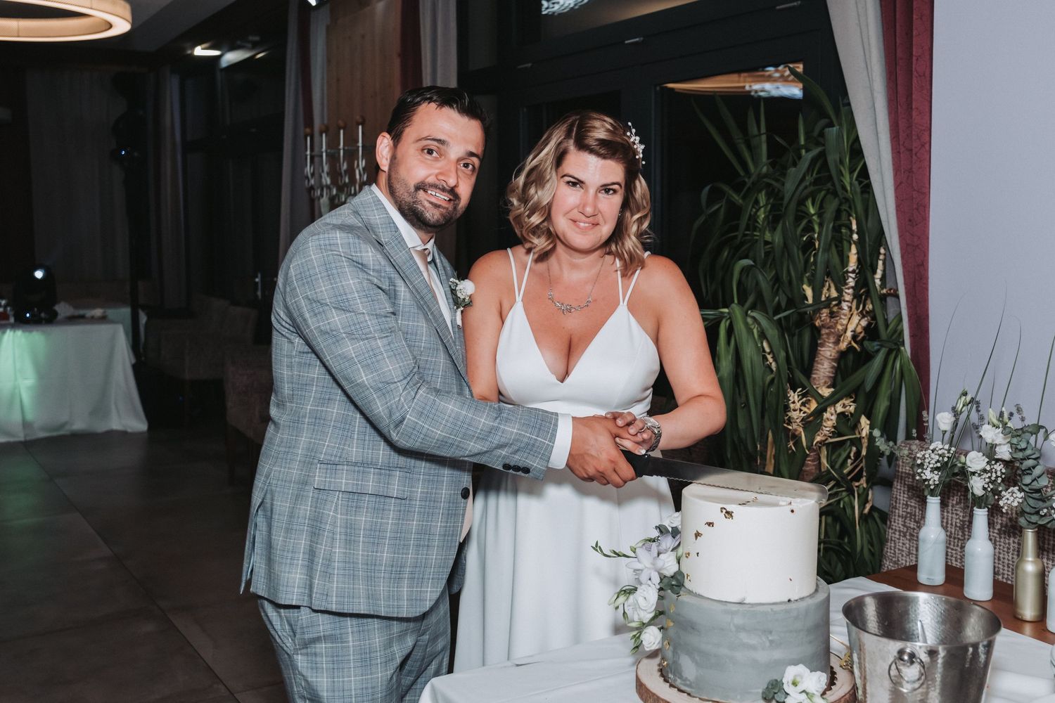 Newlyweds share a laugh while cutting their three-tiered white wedding cake.