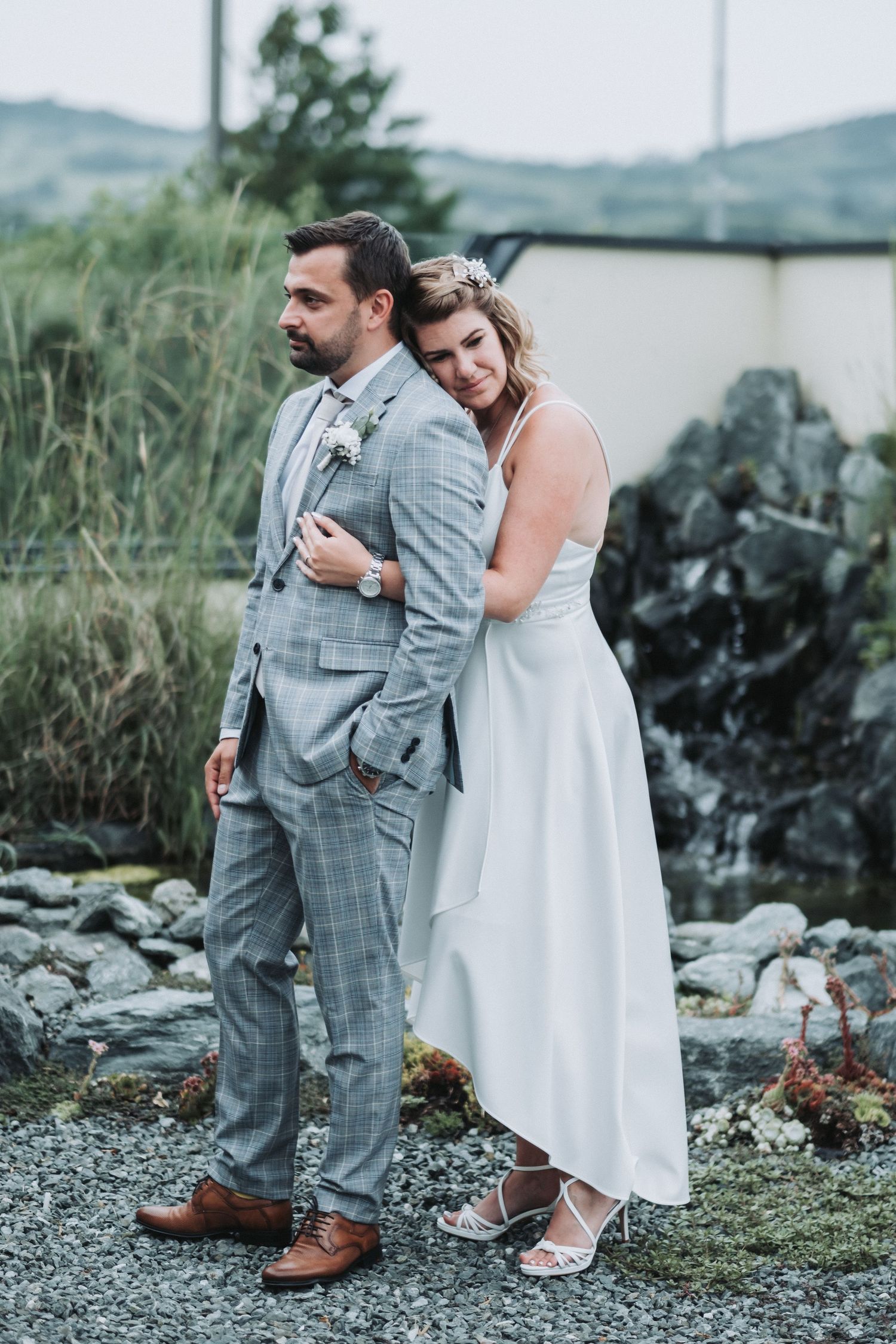 Intimate wedding portrait of couple in white dress and plaid suit embracing on rocky terrain.