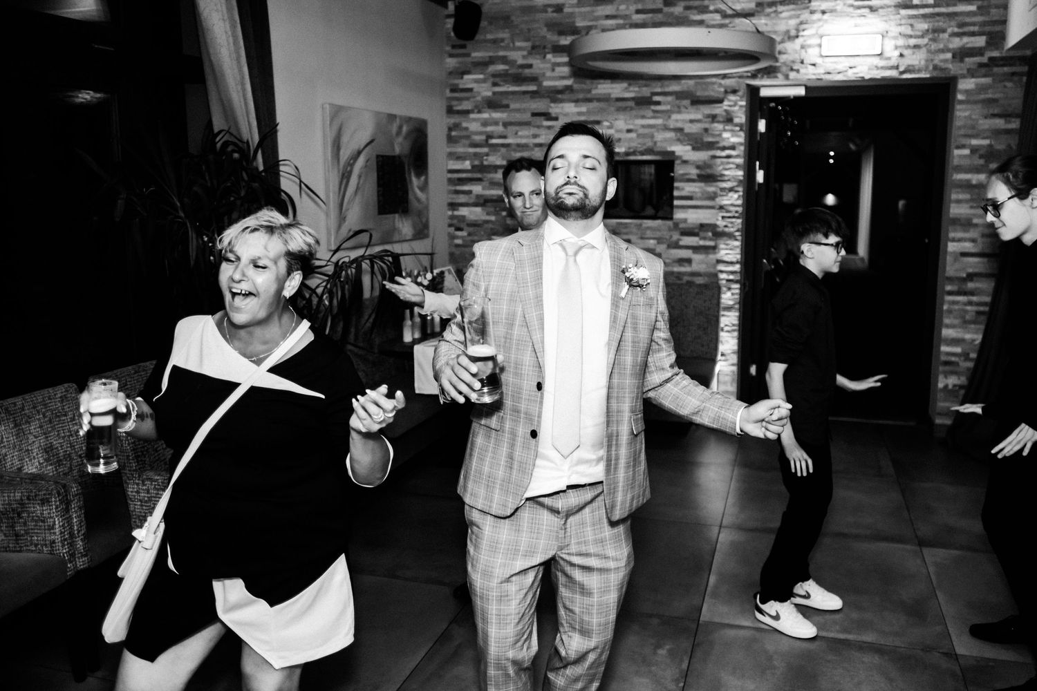 Wedding guests dancing energetically in black and white at indoor reception venue.
