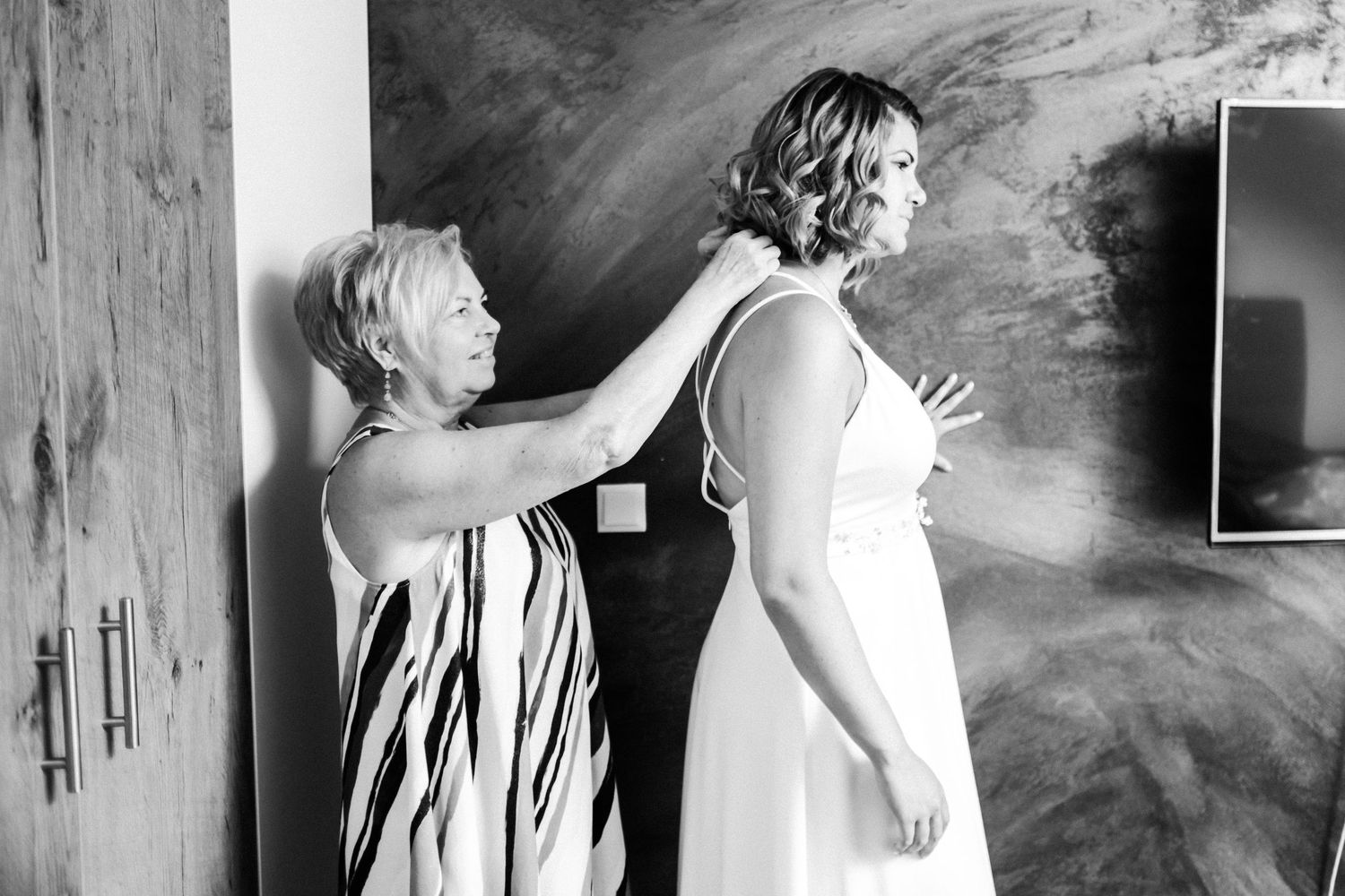A tender moment between two women during wedding preparations against a textured wall.