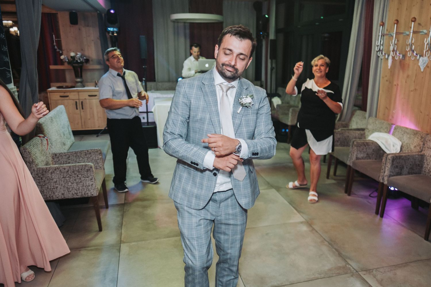 Groom in light grey checkered suit stands on dance floor during wedding reception.