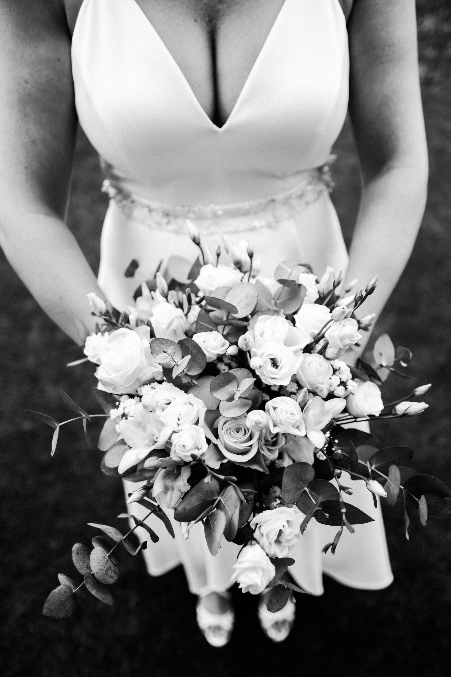 Close-up black and white photo of bridal bouquet with roses and greenery.