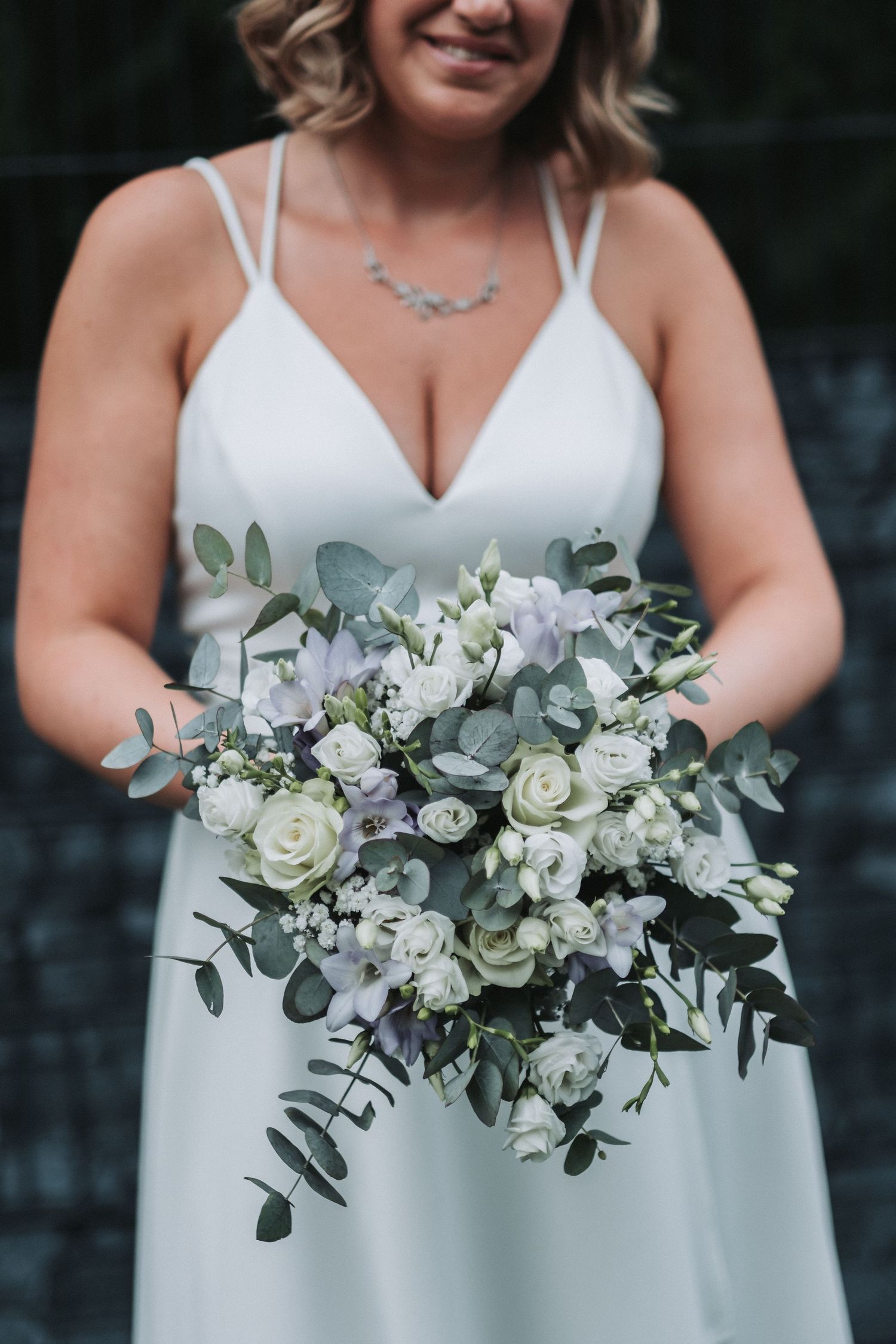 Bride in white v-neck dress holding beautiful bouquet of white roses and eucalyptus.