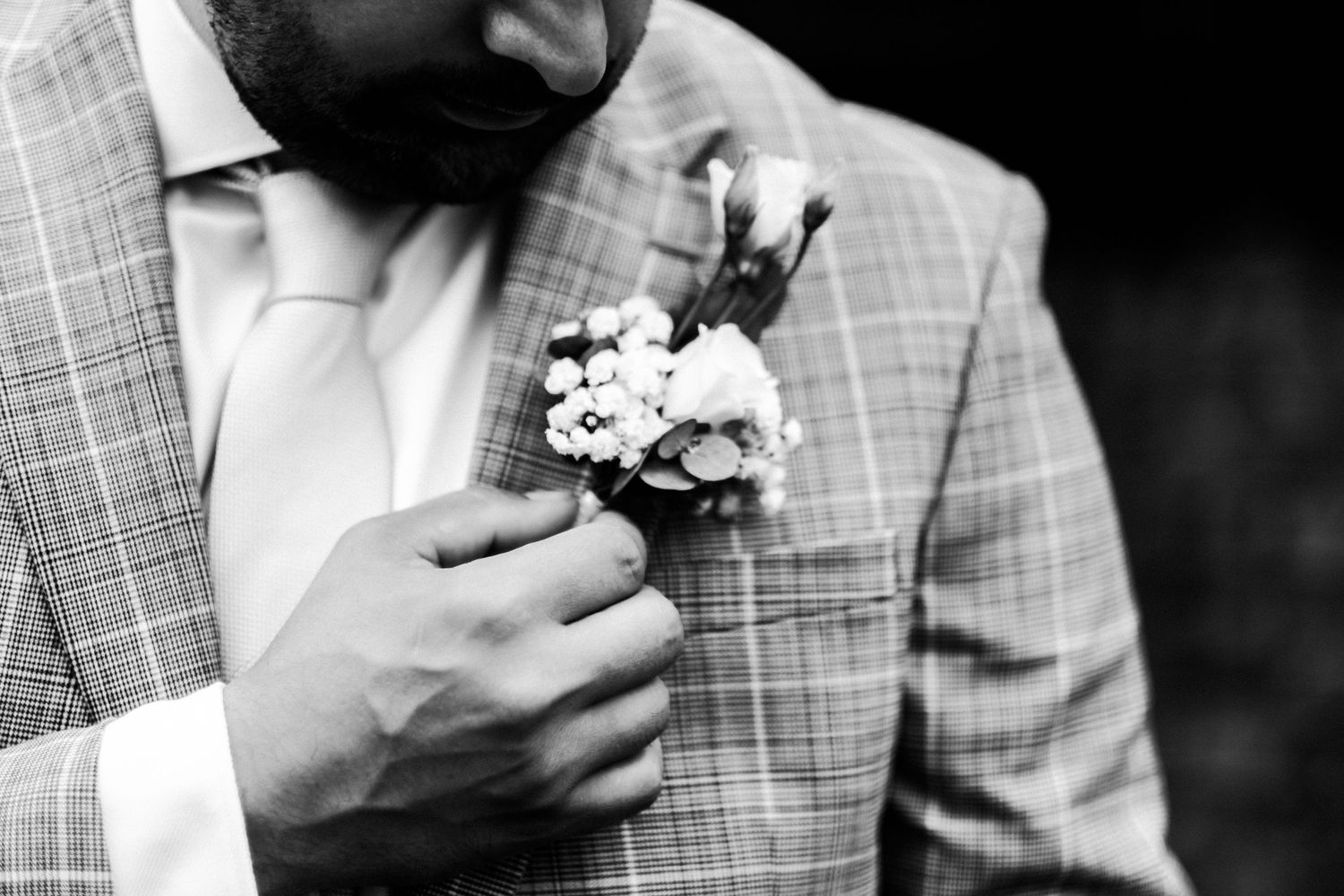 Black and white close-up of a floral boutonniere being adjusted on a checkered suit lapel.